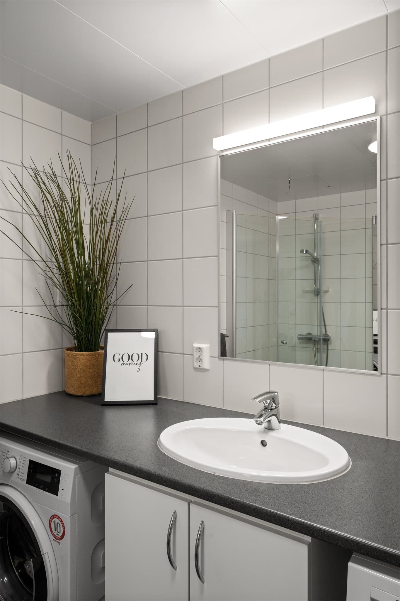 Badet er innredet med servant på skapseksjon, dusjhjørne, vegghengt toalett og opplegg for vask/tørk.