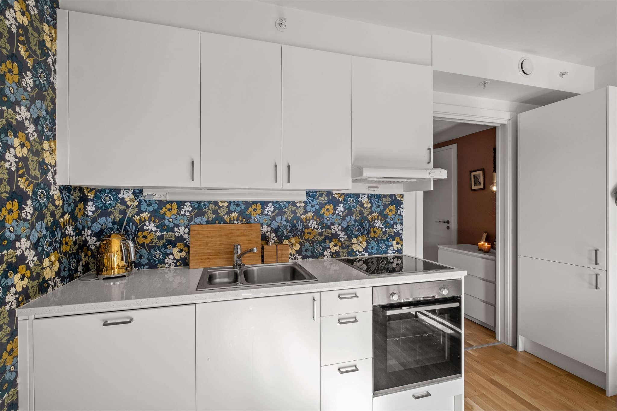 Kjøkkeninnredningen har hvite, slette fronter, laminat benkeplate og integrerte hvitevarer.