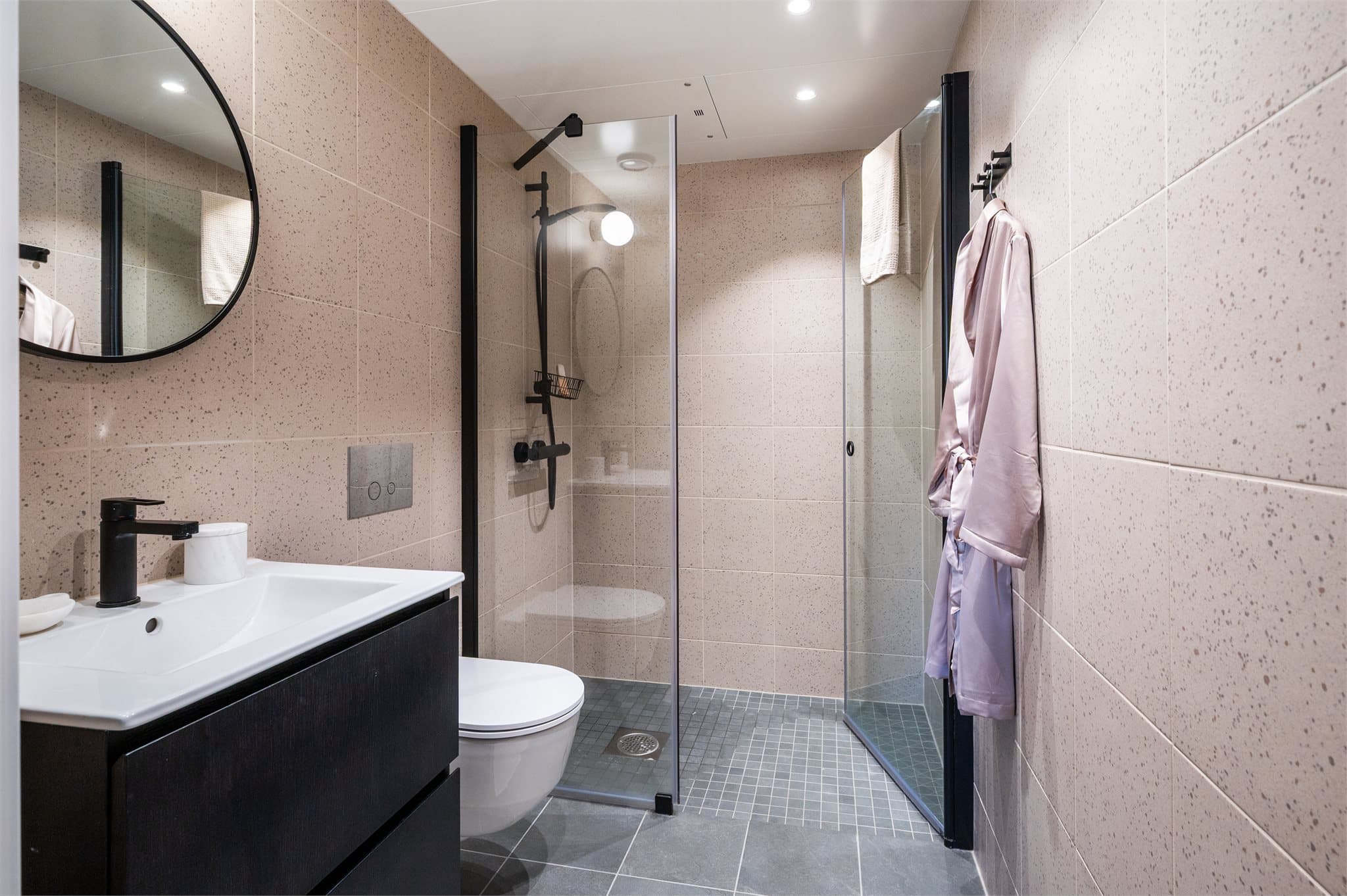 Bad med delikate beige terrazzo-fliser i flott kontrast til de grå flisene, sort armatur og dusjhjørne med glassvegger.