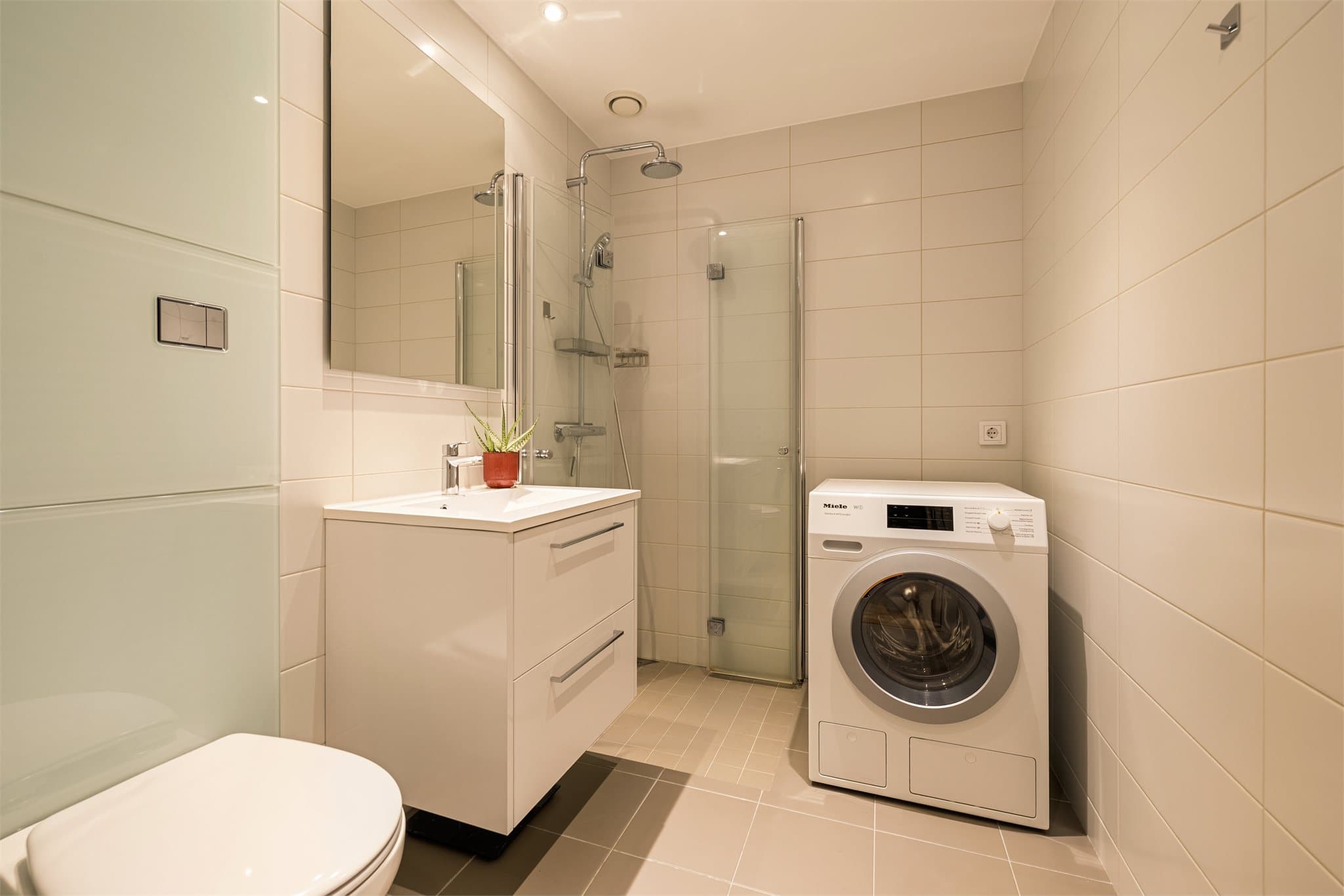 Flislagt bad med dusj og opplegg for vaskemaskin.