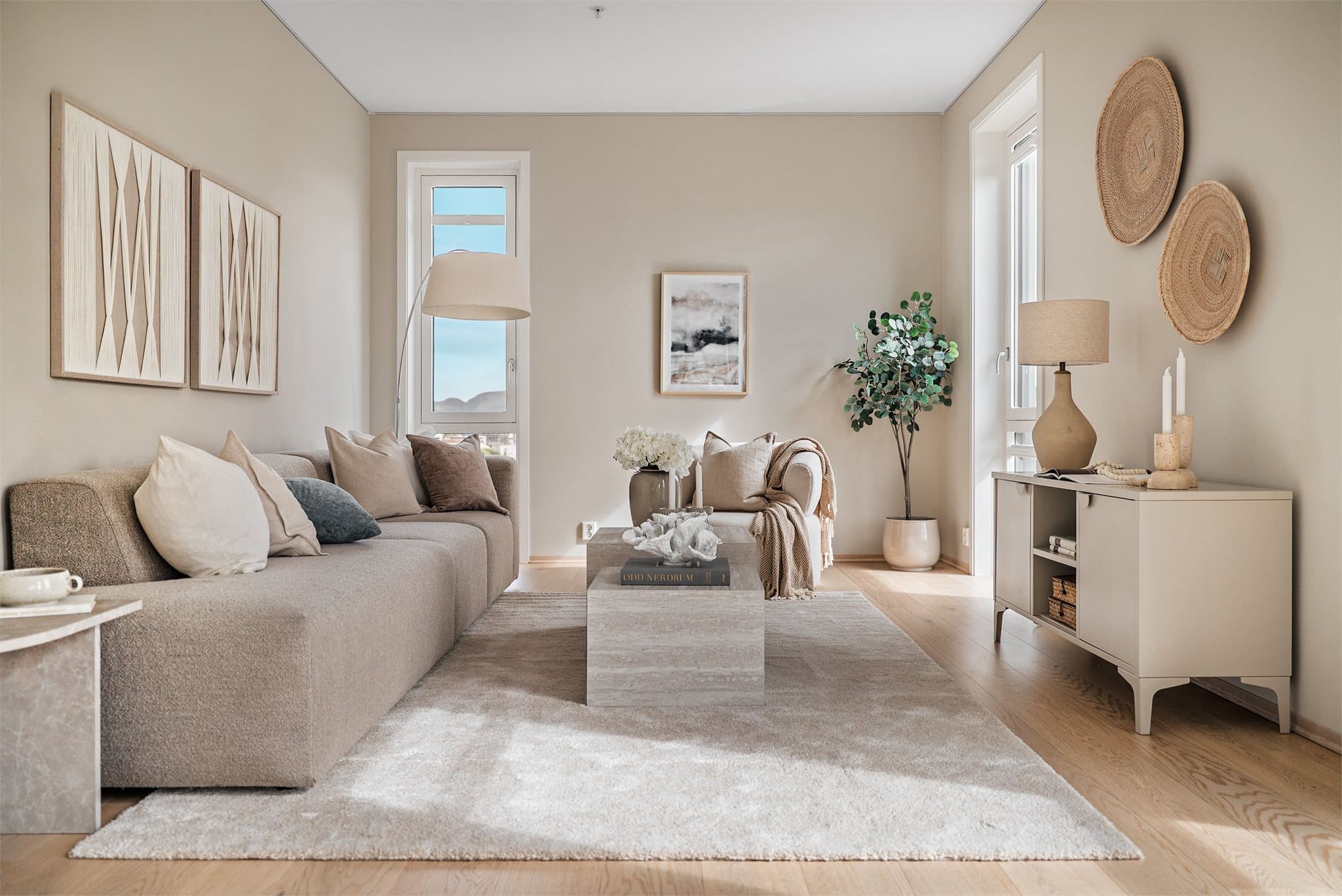 En lys og innbydende stue med lune beige fargetoner og store vindusflater som slipper inn rikelig med dagslys.