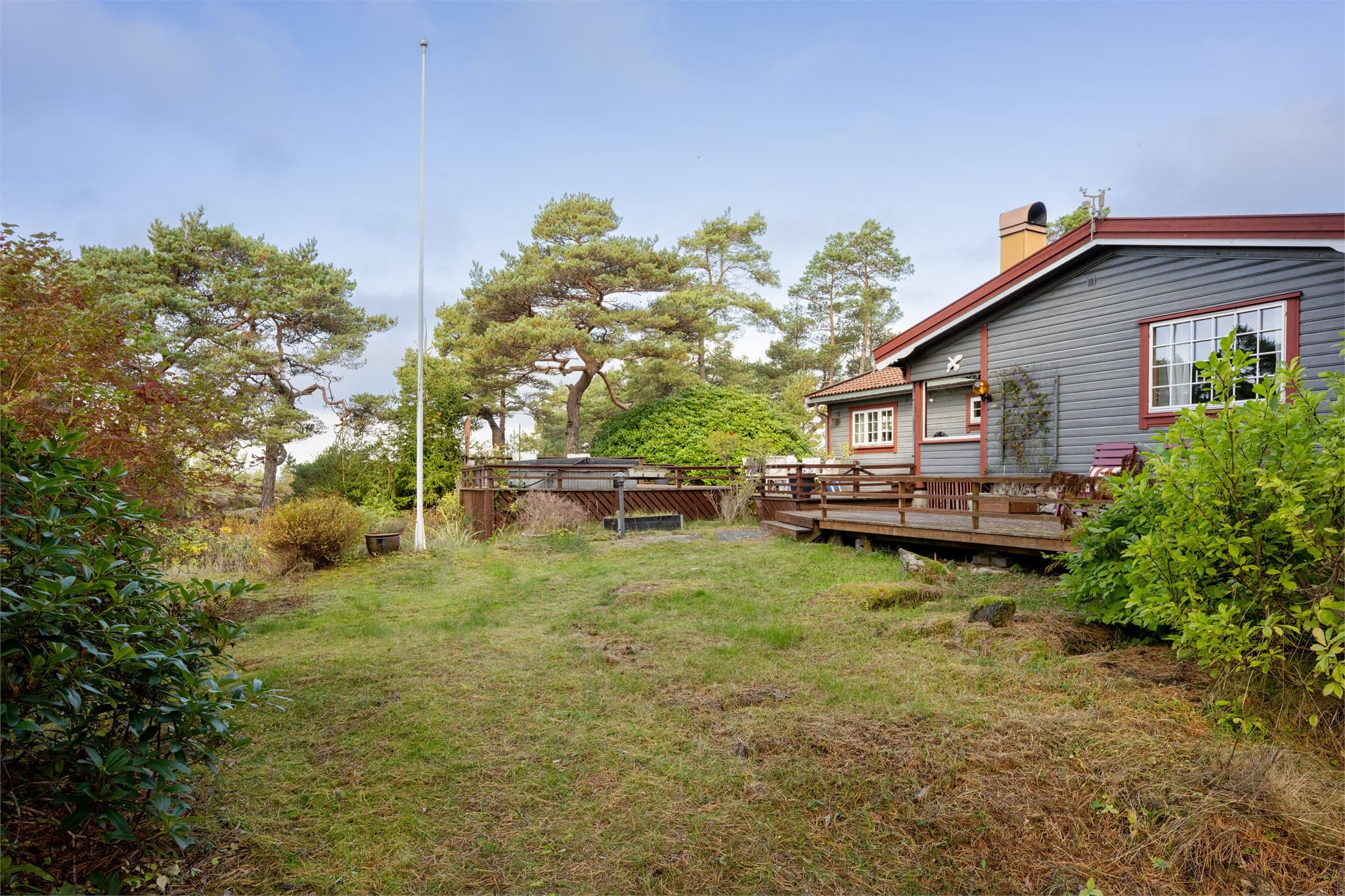 Skjermet hageområde med flaggstang og beplantning.