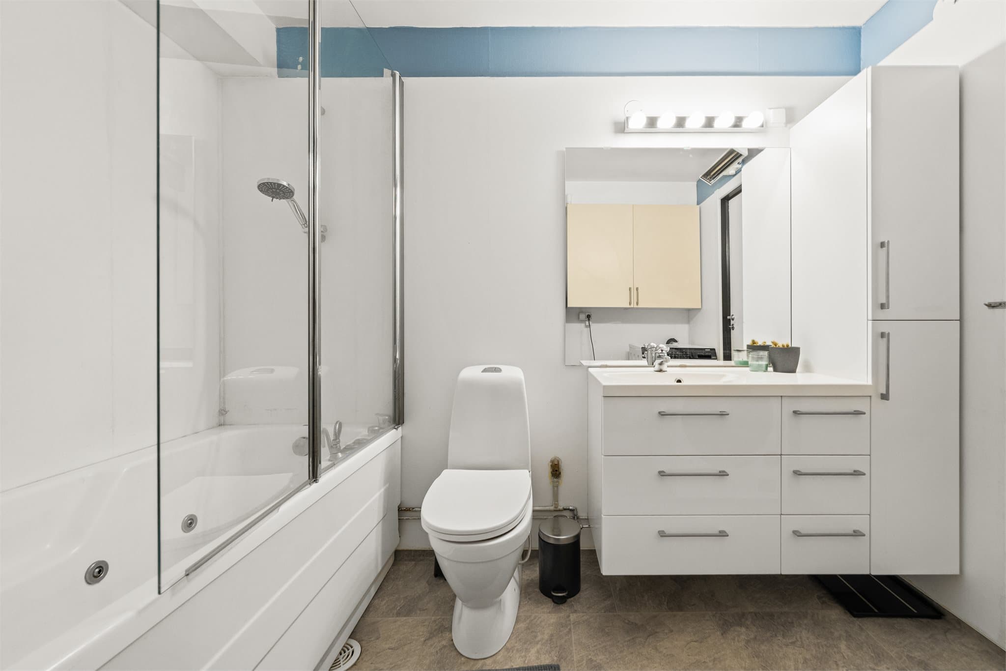 Lyst baderom med pen og tidløst baderomsinnredning, gulvstående toalett og badekar med glassfelt.