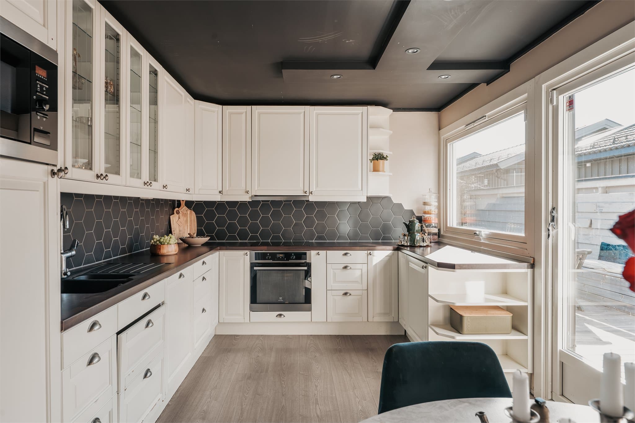 Innredningen har profilerte, fabrikklakkerte fronter og laminat benkeplate med planlimt kum i kompositt. Det er "Hexagon" fliser på vegg over benkeplate. Belysning via downlights under overskap.