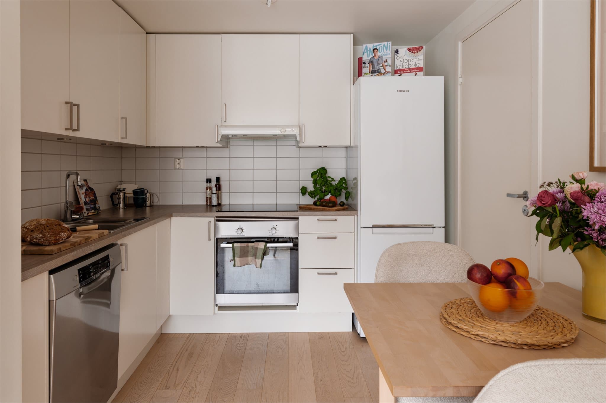 Lyst, tidløst kjøkken med plass til spisebord mellom sonene.