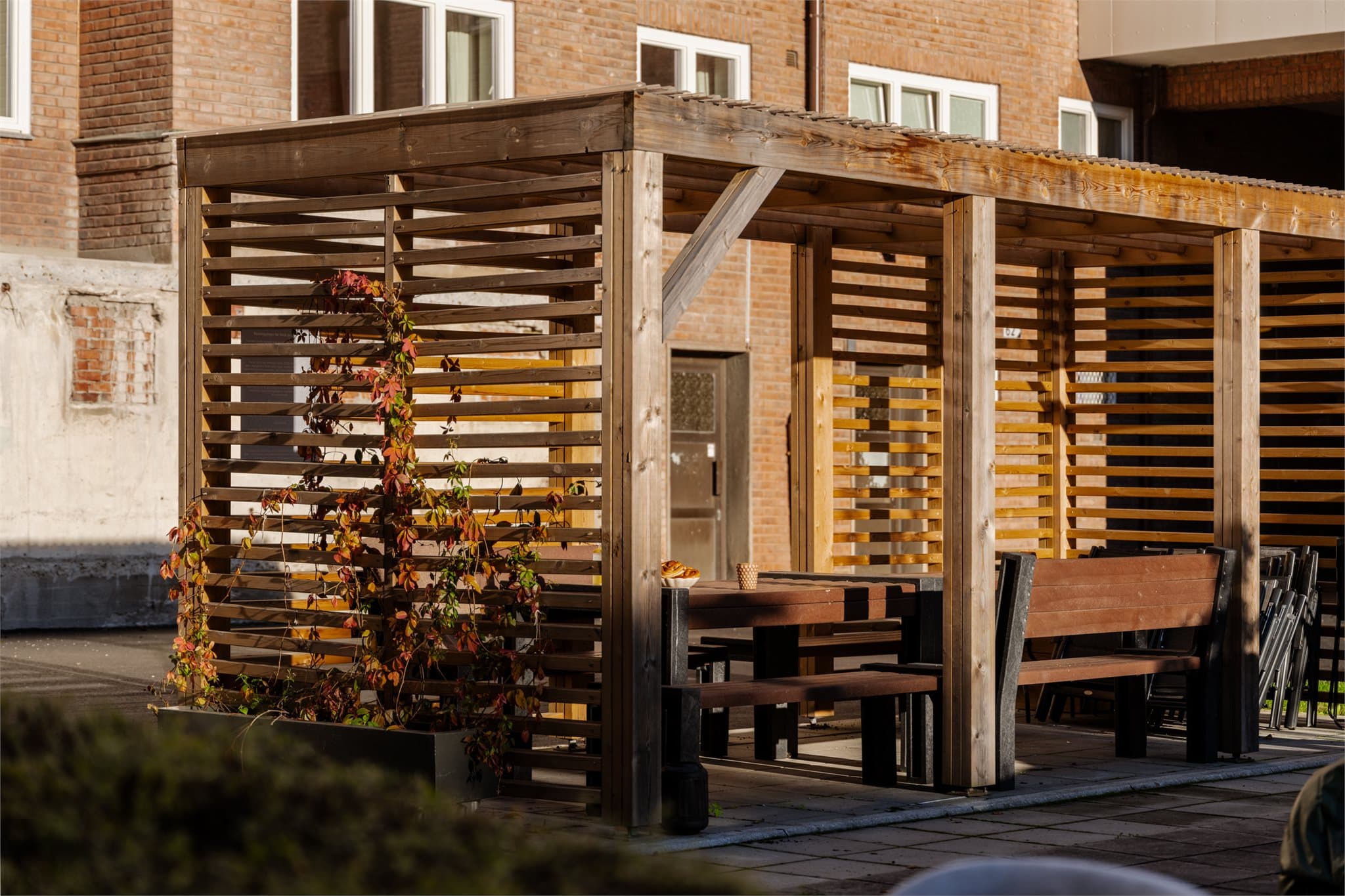 Pergola med faste sittebenker og langbord i bakgården.