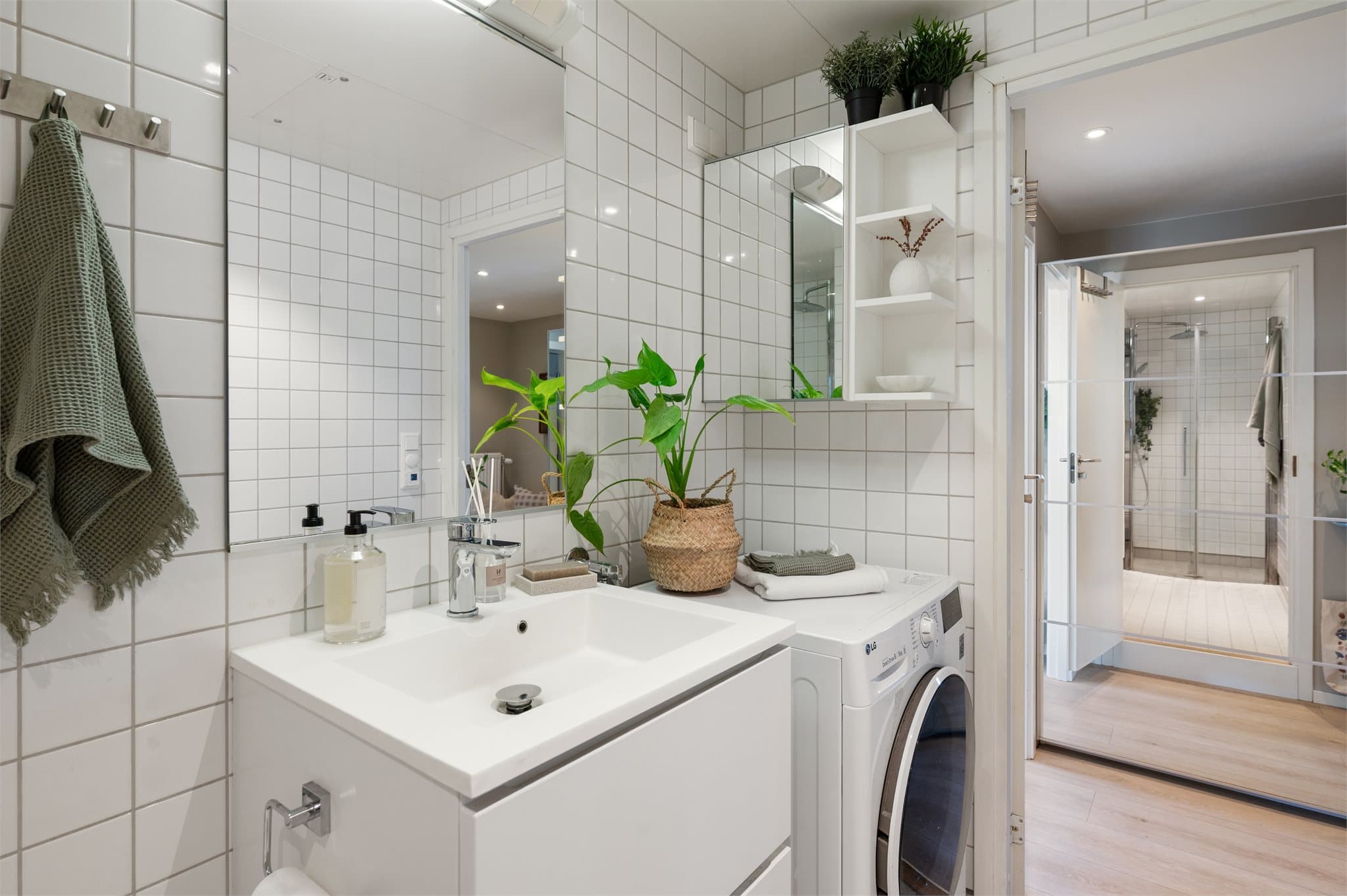 Lyst og moderne bad som er innredet med hvite fliser, servant med skuffer og speil med lys over.