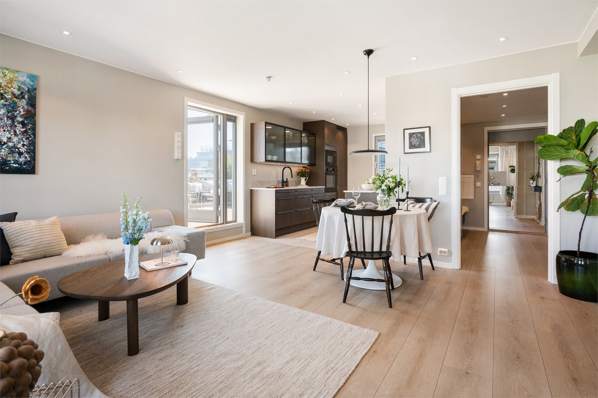 Åpen stue- og kjøkkenløsning med lys innredning, spiseplass og utgang til terrasse.