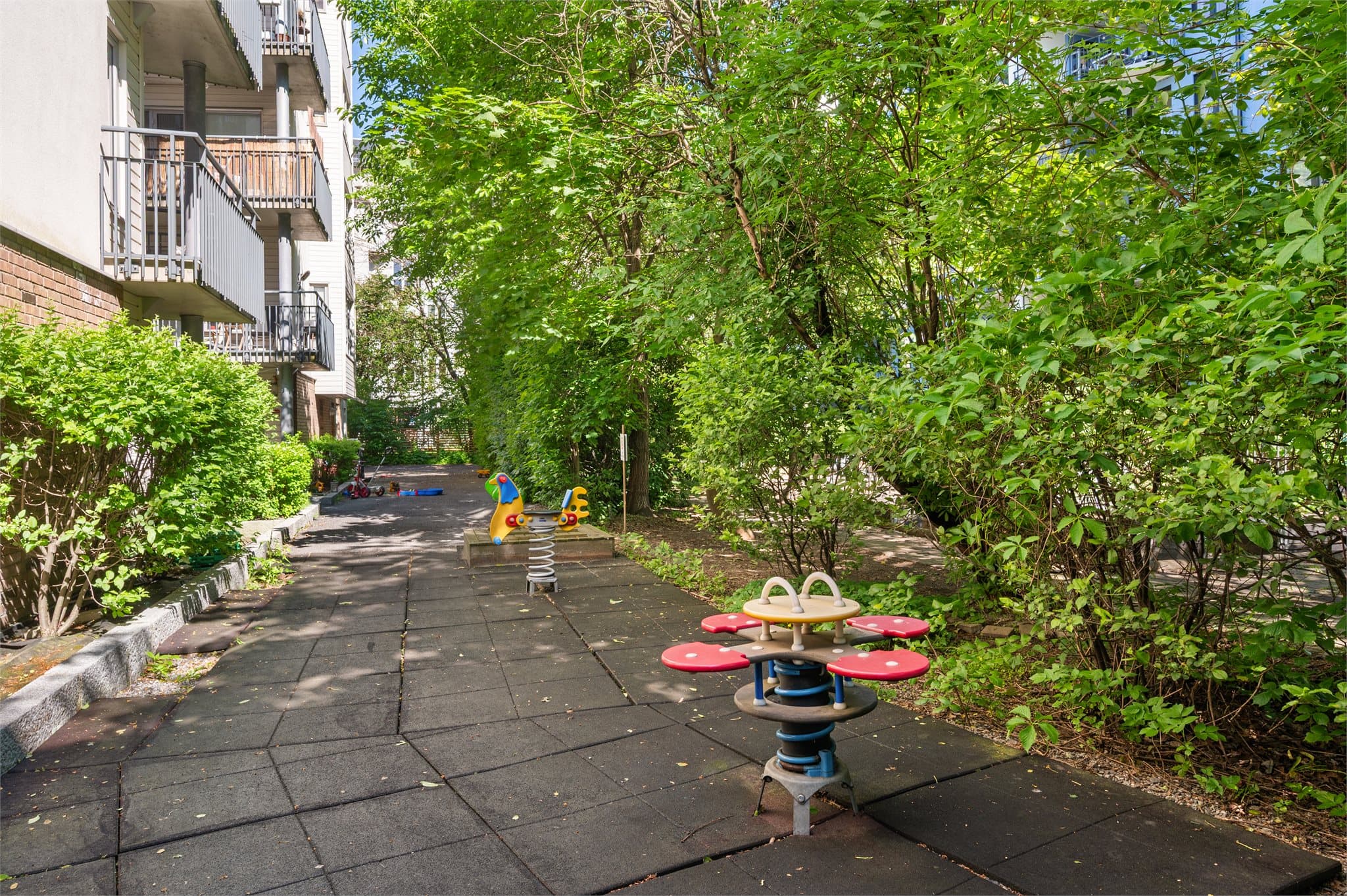 Lekeområde med husker og sitteplasser. Grønne busker og trær omkranser området.