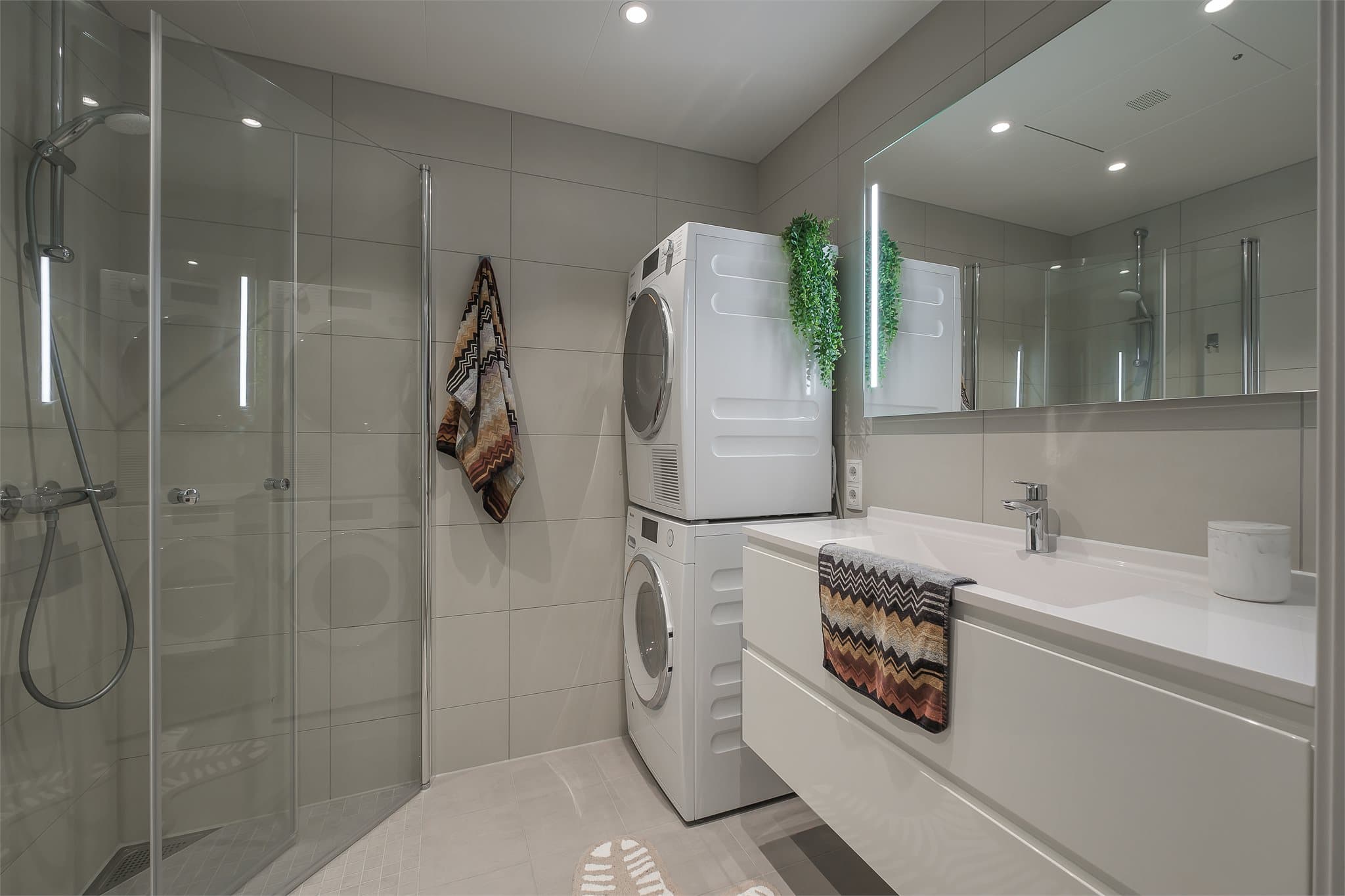 Lyst og delikat baderom utstyrt med stor servantinnredning, speil med lys, dusjhjørne og vegghengt toalett, samt opplegg for vaskemaskin.