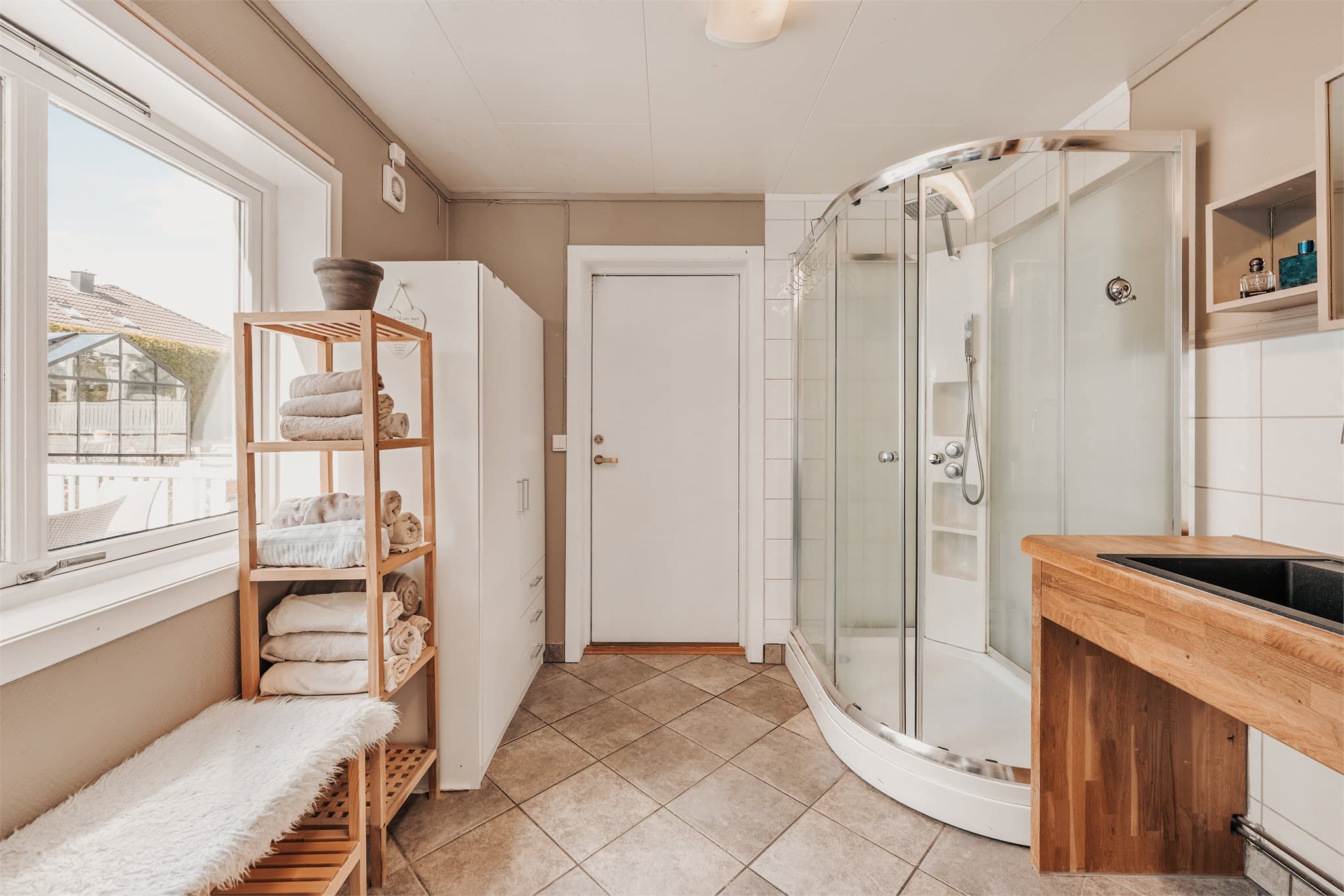 Badet i 1.etasje har fliser på gulv og er innredet med servant, toalett og dusjkabinett.