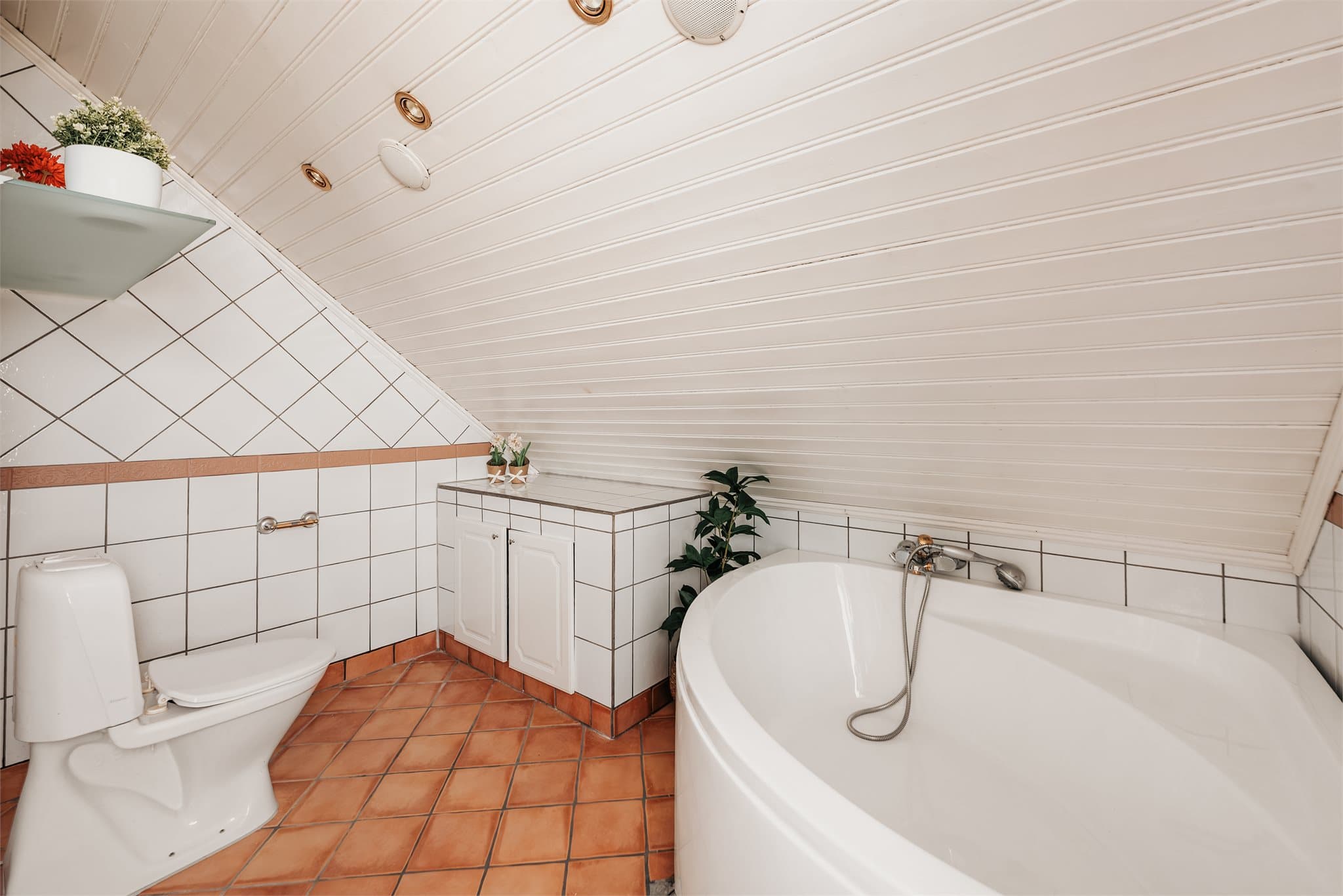 Badet er innredet med hjørnebadekar, toalett og dobbeltservant på underskap.
