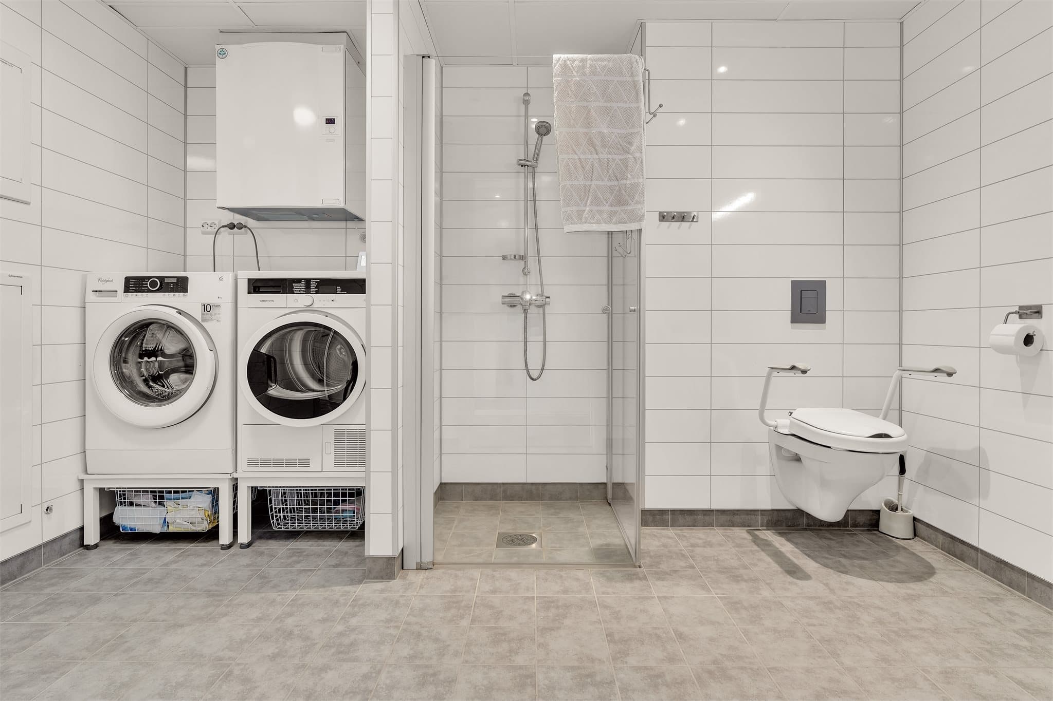 Flislagt bad med vannbåren gulvvarme, nedsenket dusjsone og opplegg for vaskemaskin.