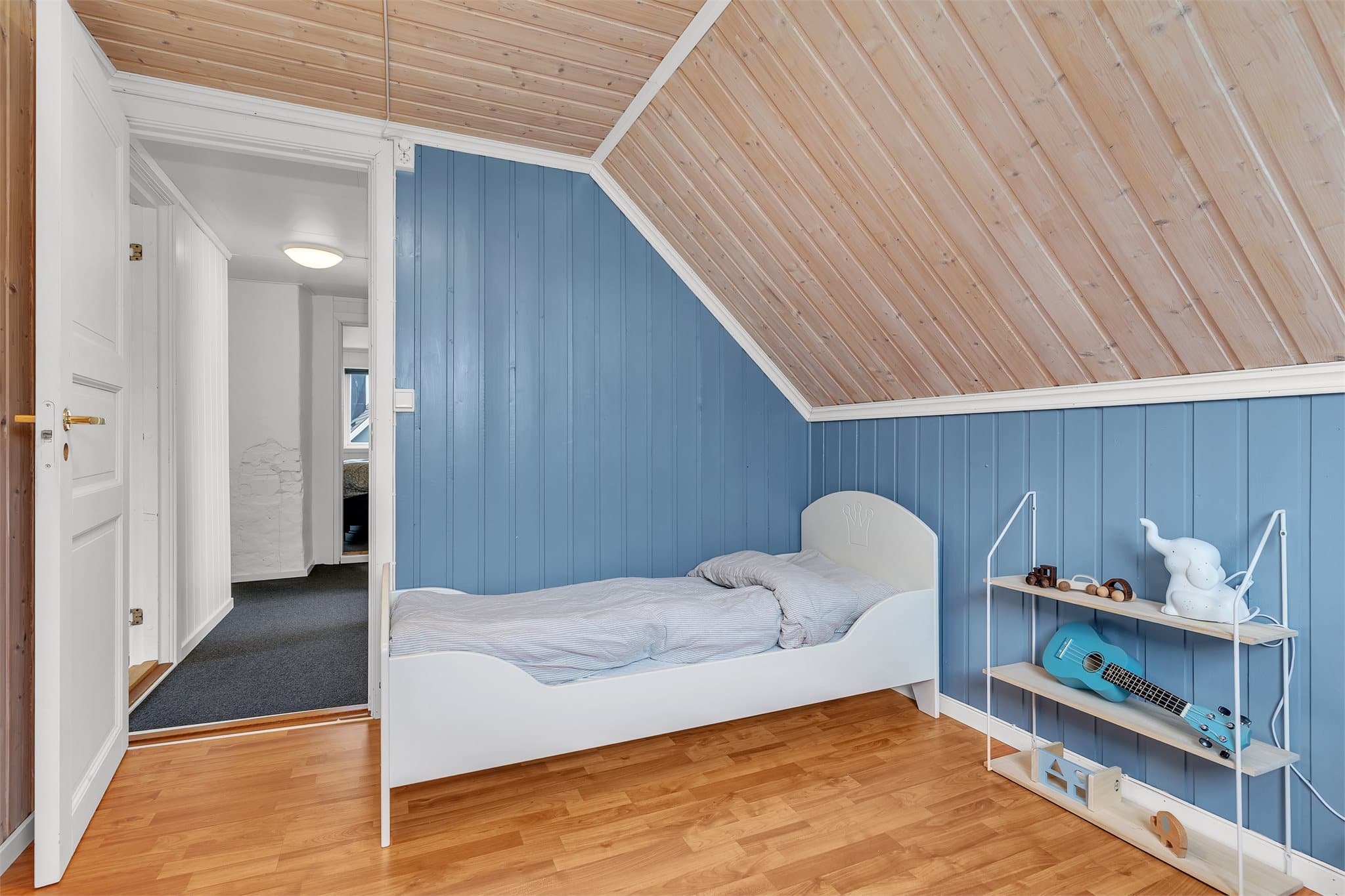 Soverom med laminatgulv og vegger med malt trepanel.