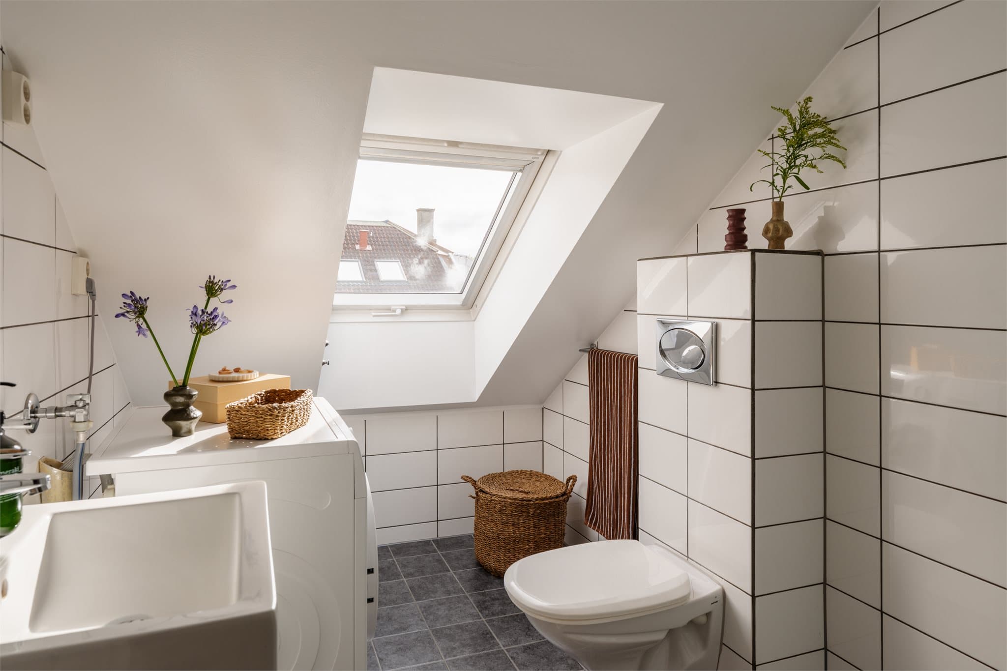 Flislagt baderom med varmekabler i gulv, takvindu, vegghengt toalett og opplegg for vaskemaskin.