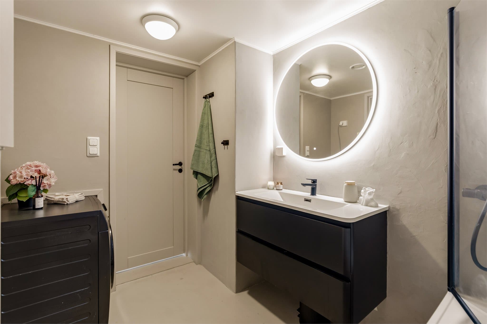 Badet er innredet med baderomsinnredning med skuffer, servant, speil med integrert belysning, badekar med dusjløsning, vegghengt toalett og opplegg for vaskemaskin.