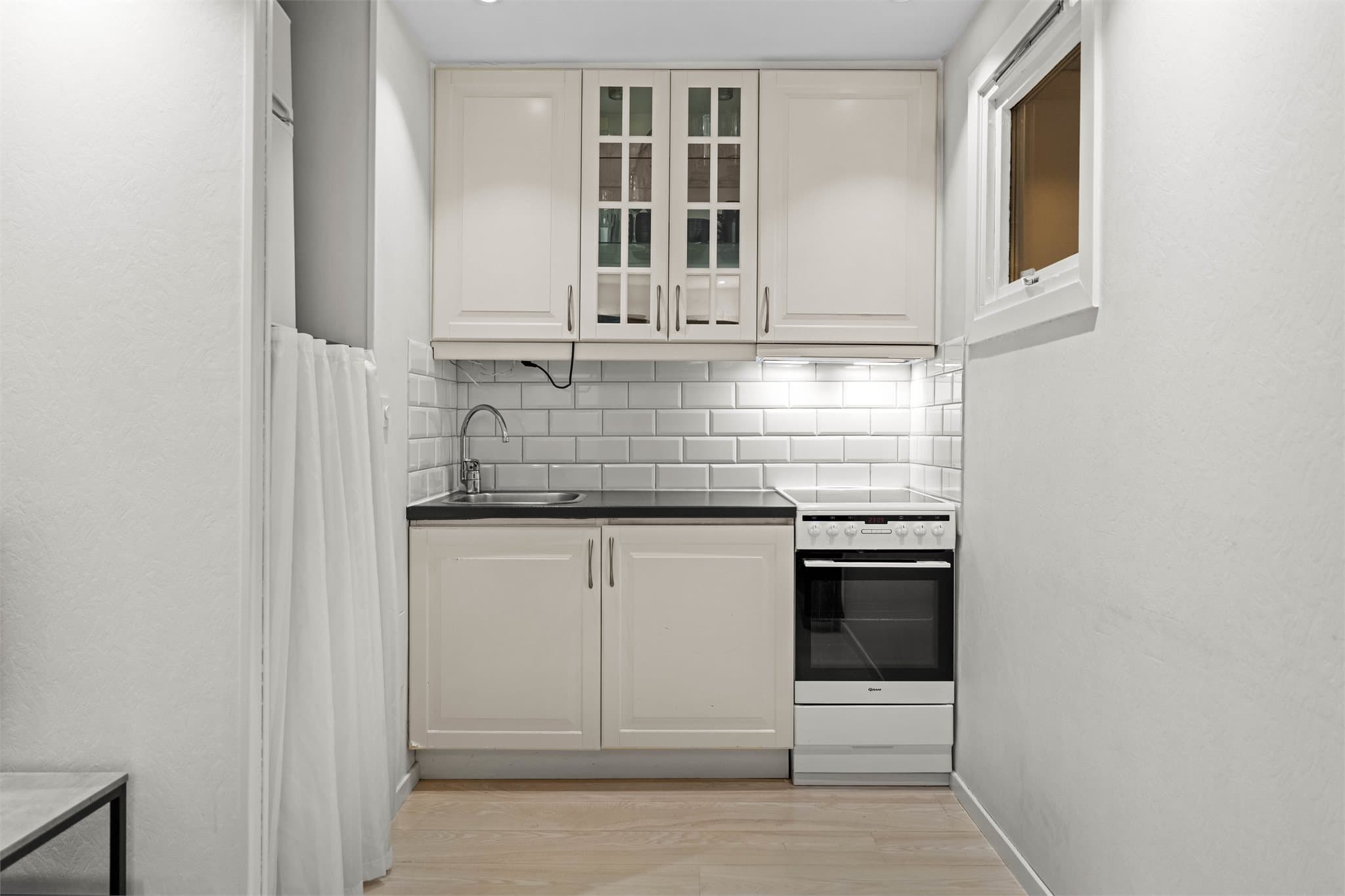 Kjøkkeninnredning med profilerte fronter og enkelte overskap med glassfronter. Fliser på vegg over benkeskap, laminat benkeplate med nedfelt oppvaskkum i rustfritt stål samt ventilator over kokesone.