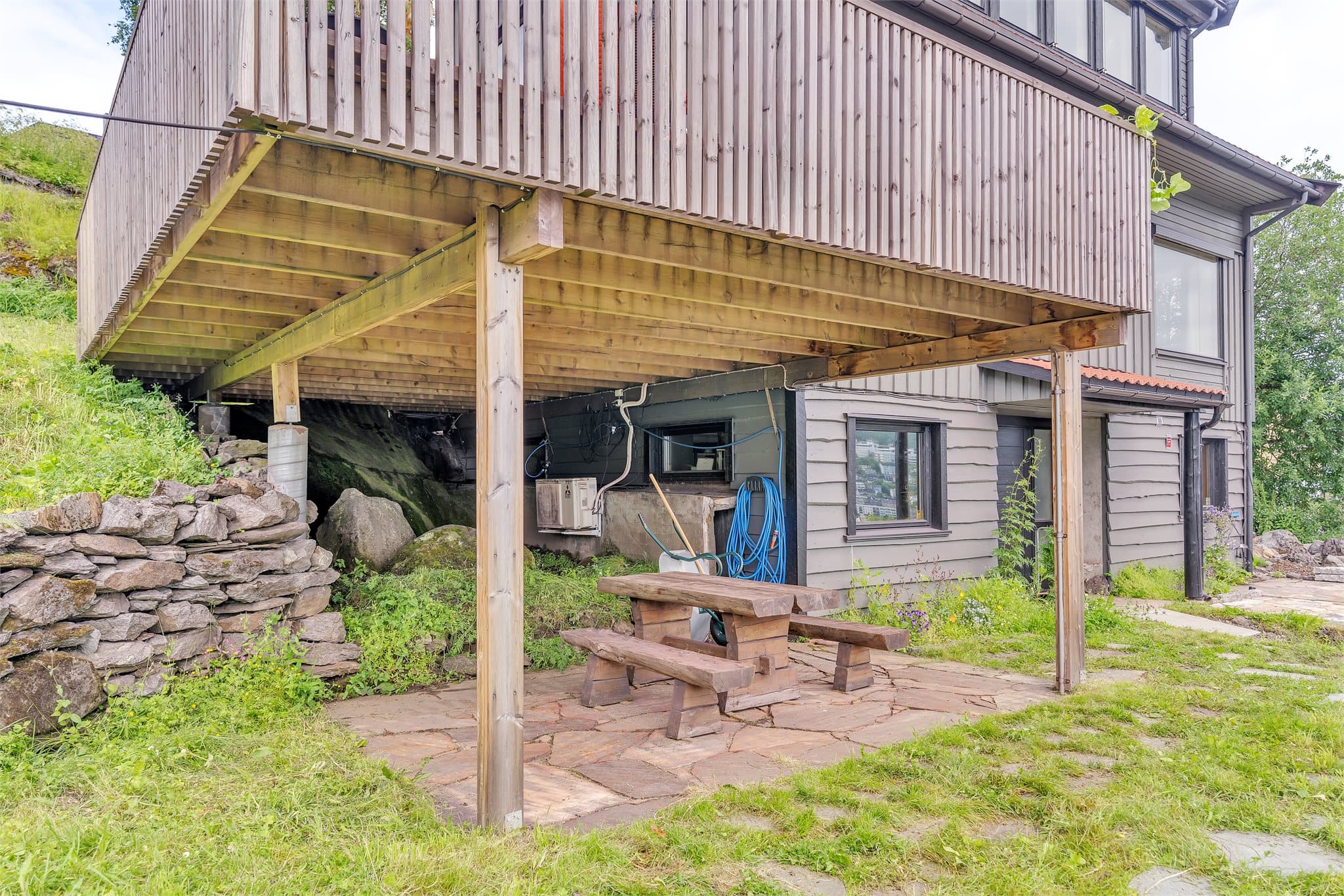 Overbygd uteplass under verandaen med skiferheller og tørrmur i naturstein.