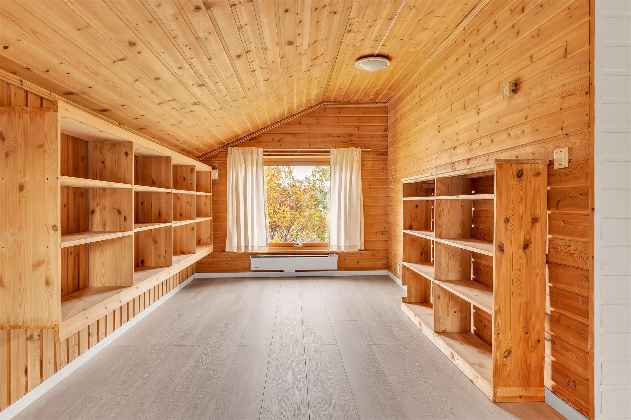 Bibliotek/loftstue innredet med plassbygde trehyller langs begge vegger og furupanel.