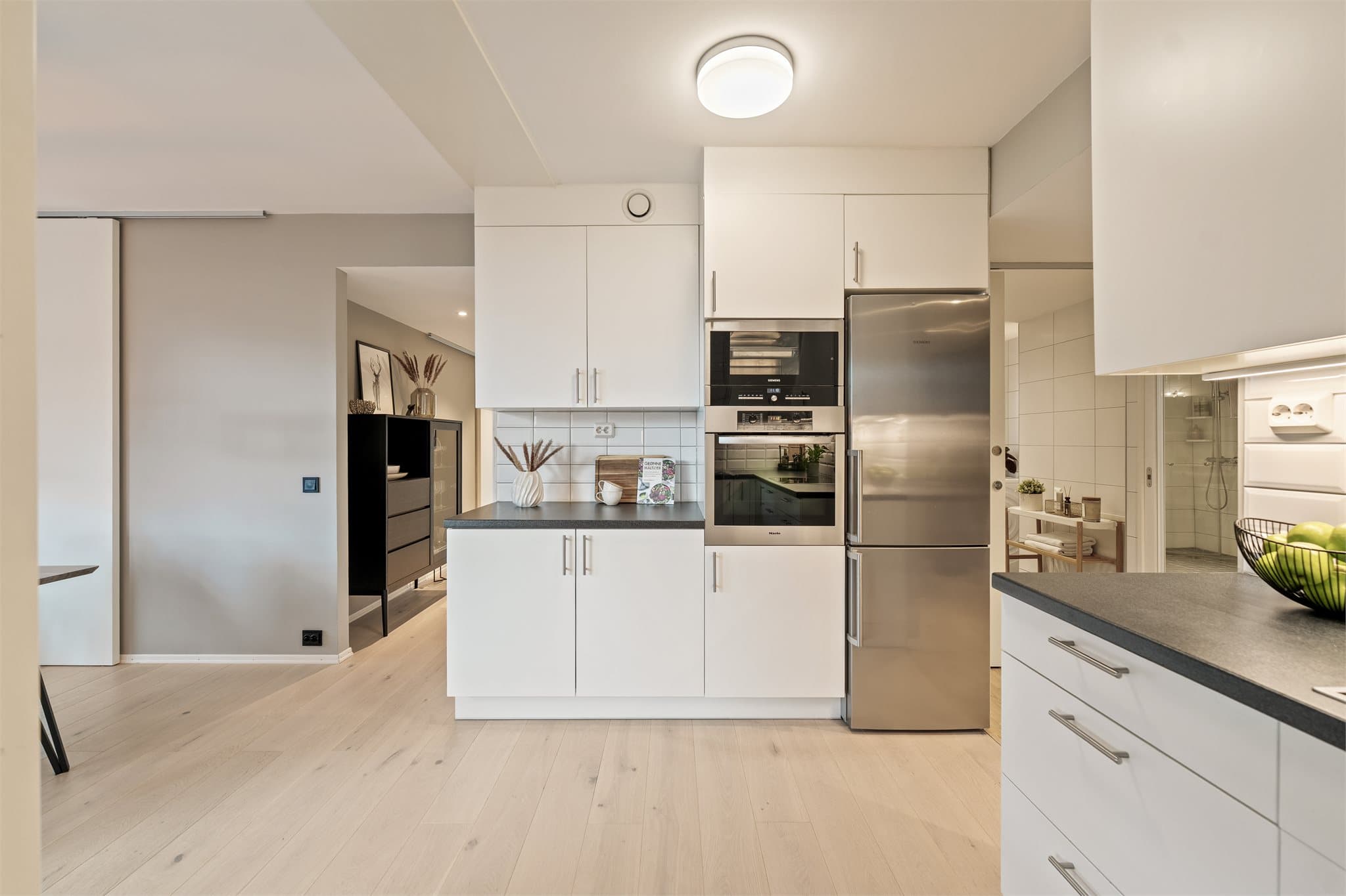 Tidløs kjøkkeninnredning med slette fronter og laminat benkeplate. Det er integrerte hvitevarer som induksjonstopp, stekeovn og dampovn. Ellers frittstående kjøl/frys og oppvaskmaskin.