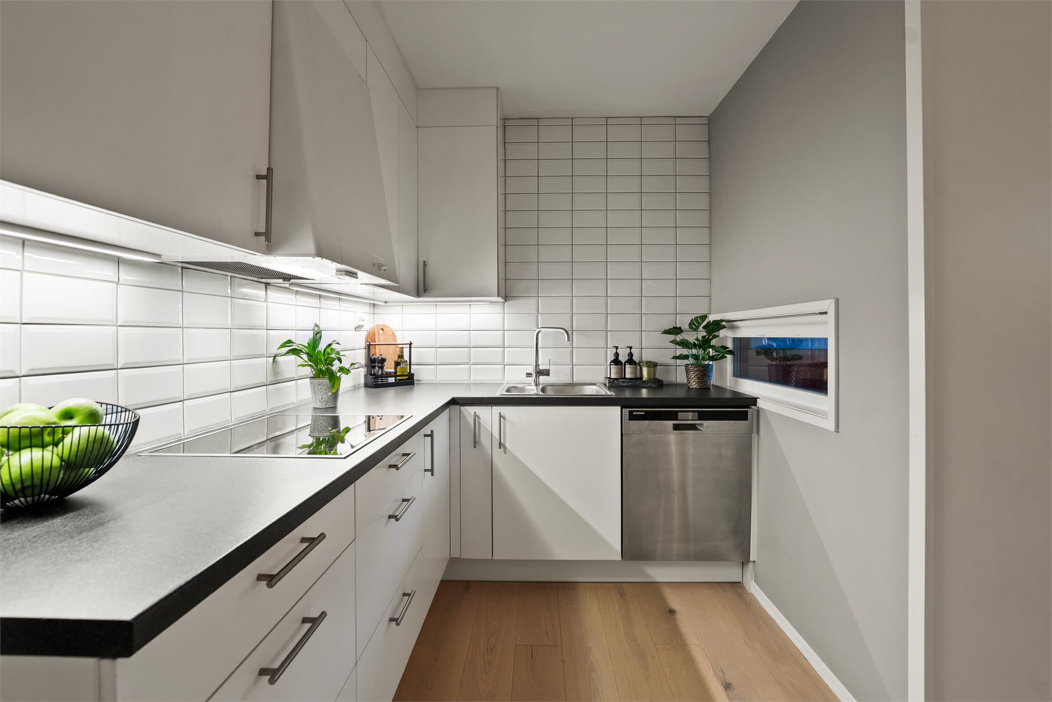 Videre har kjøkkenet nedfelt oppvaskkum med ett-greps armatur, fliser på vegg over kjøkkenbenk og benkeskapsbelysning og stikkontakter over benkeplate.