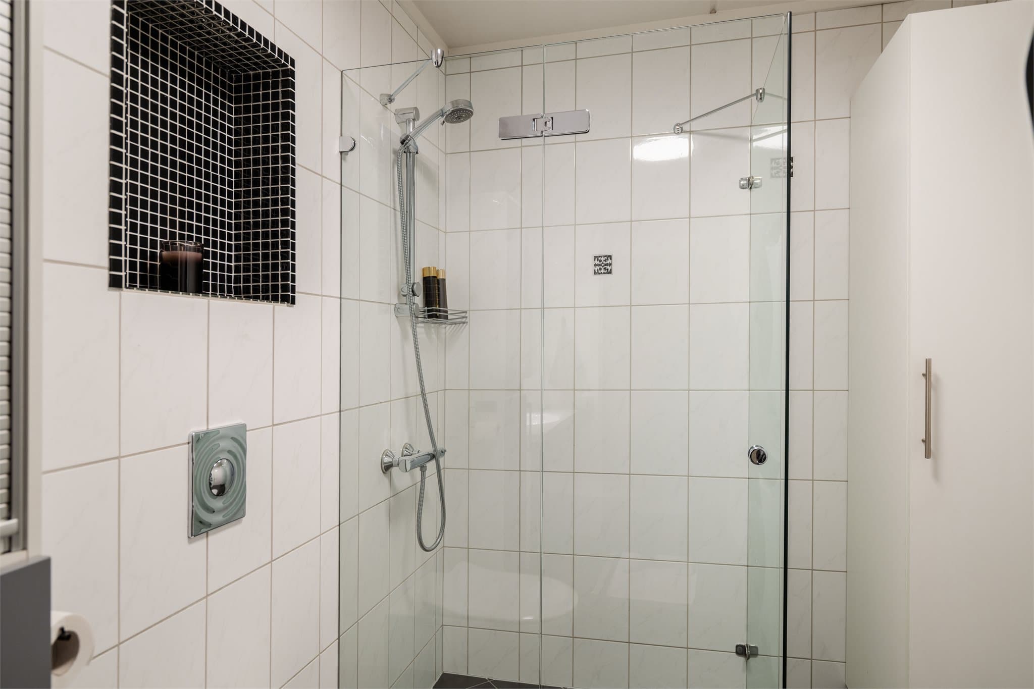 Romslig dusjplass med dusjdører i herdet glass, samt en praktisk innfelt hylle for oppbevaring av baderomsartikler.