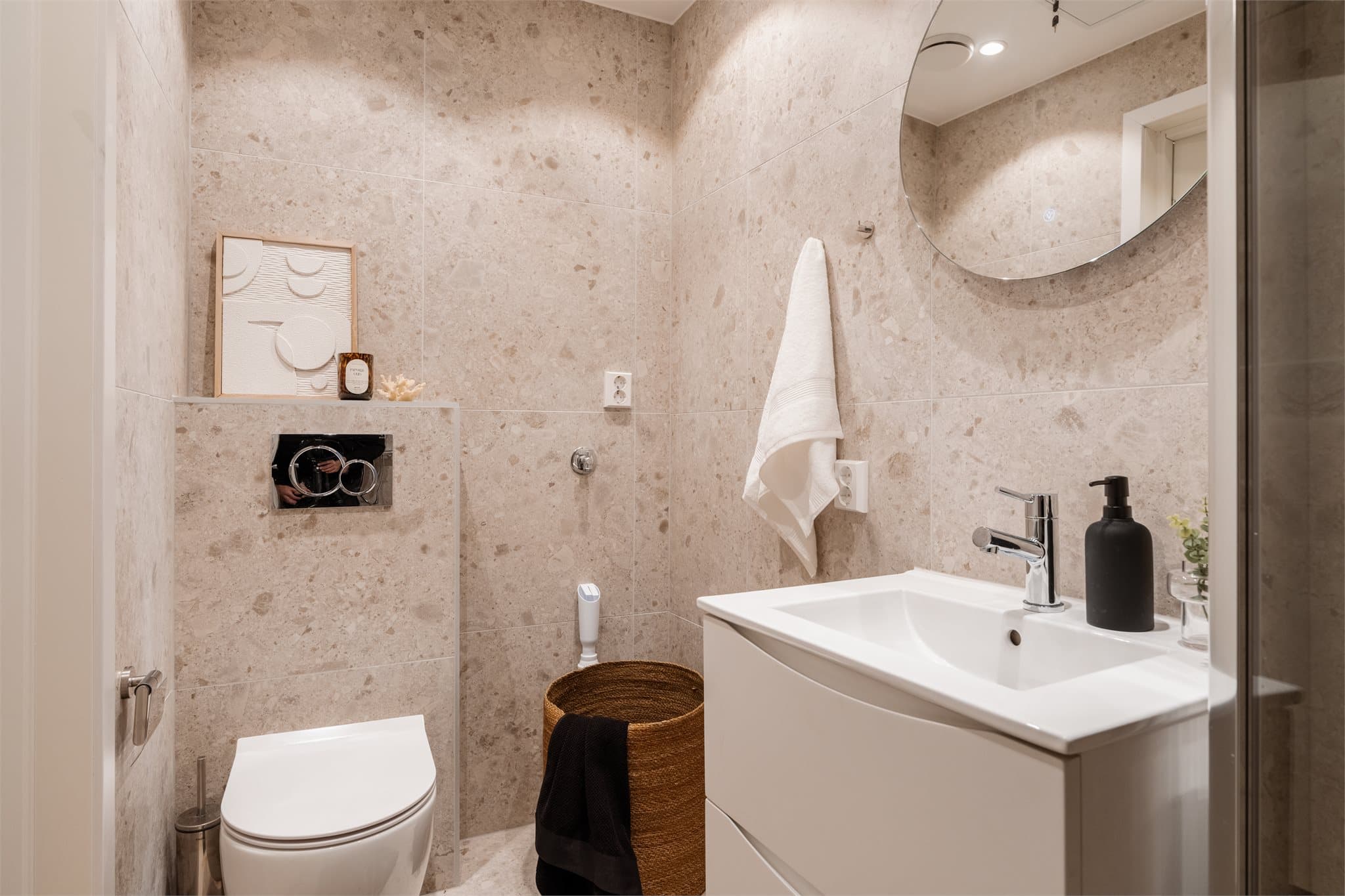 Badet har en stilren servant med møbel, speil og opplegg for vaskemaskin.