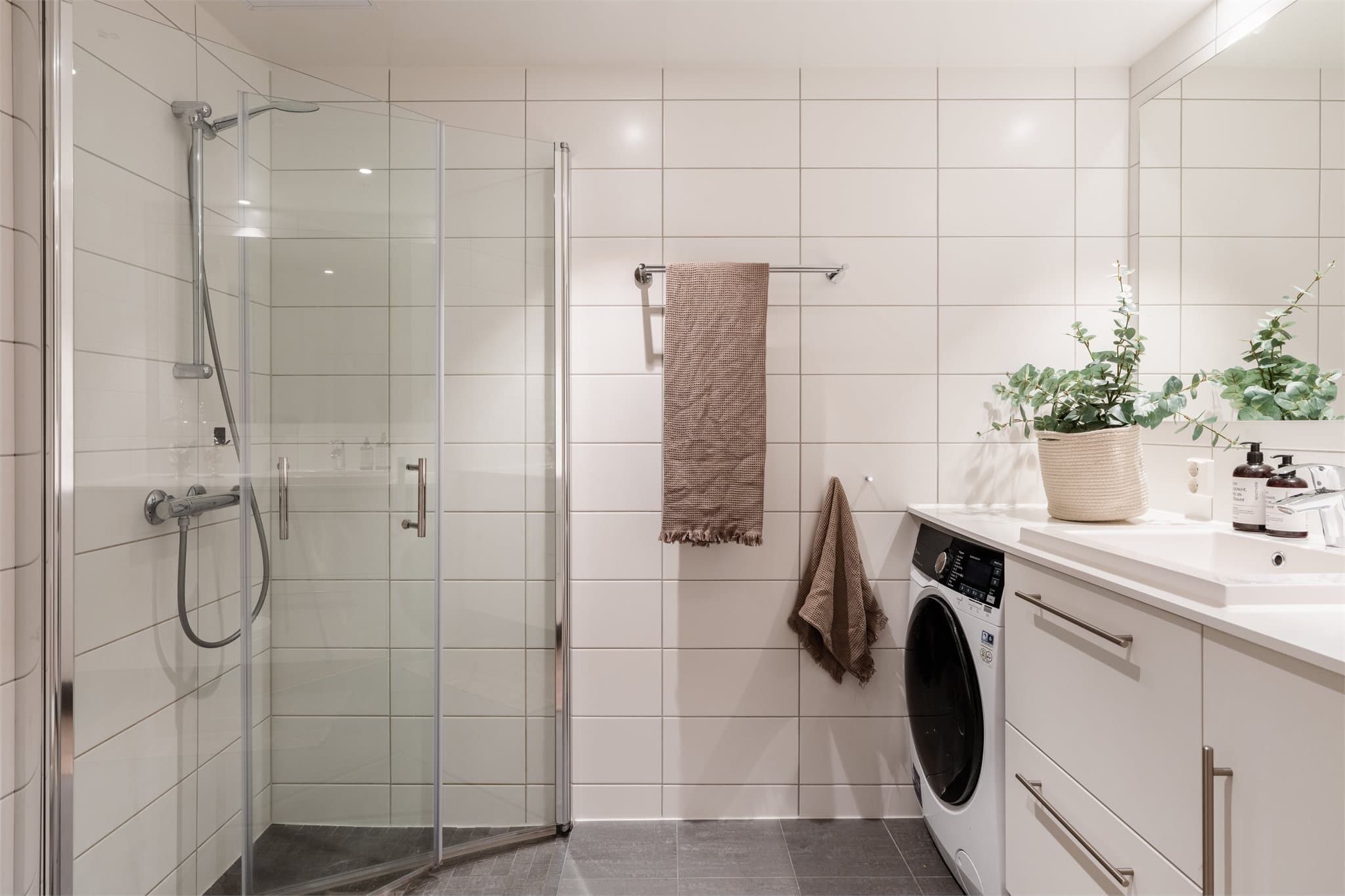 Pent baderom med flislagte overflater, vannbåren gulvvarme og opplegg for vaskemaskin.