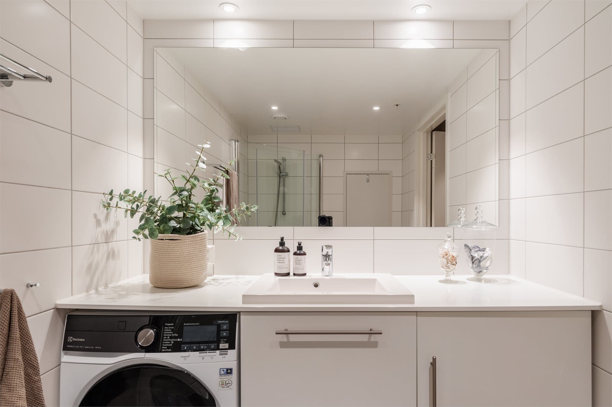 Badet har veggmontert toalett og dusjnisje med innfellbare glassdører.