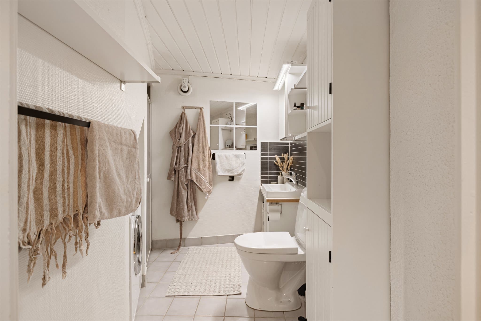 Lyst bad med toalett, dusjnisje, servantinnredning og opplegg for vaskemaskin.