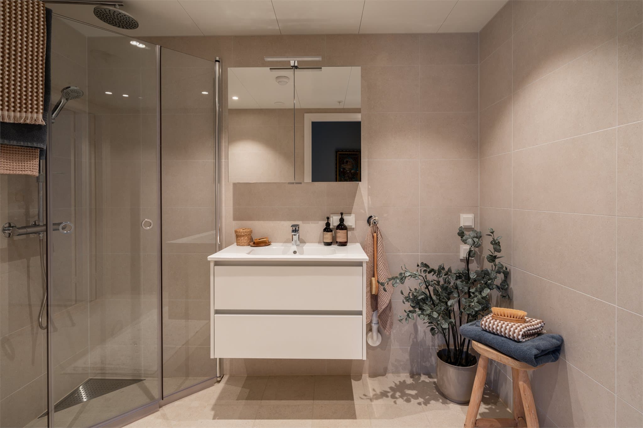 Badet er utstyrt med moderne servantinnredning, speilskap med belysning, dusjhjørne med innfellbare dører og vegghengt toalett, samt opplegg for vaskemaskin.