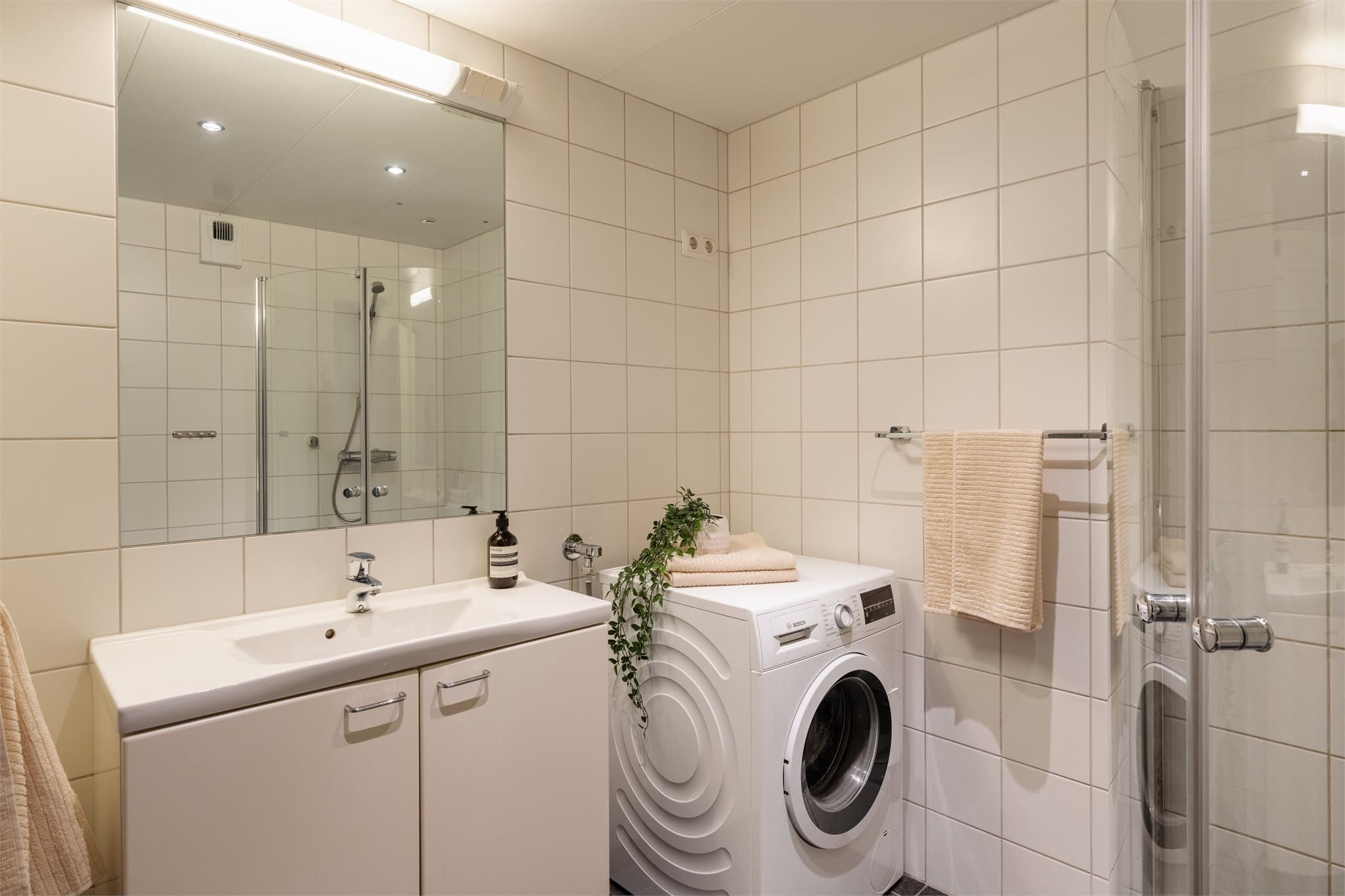 Badet er innredet med servant, dusjhjørne og opplegg for vaskemaskin.