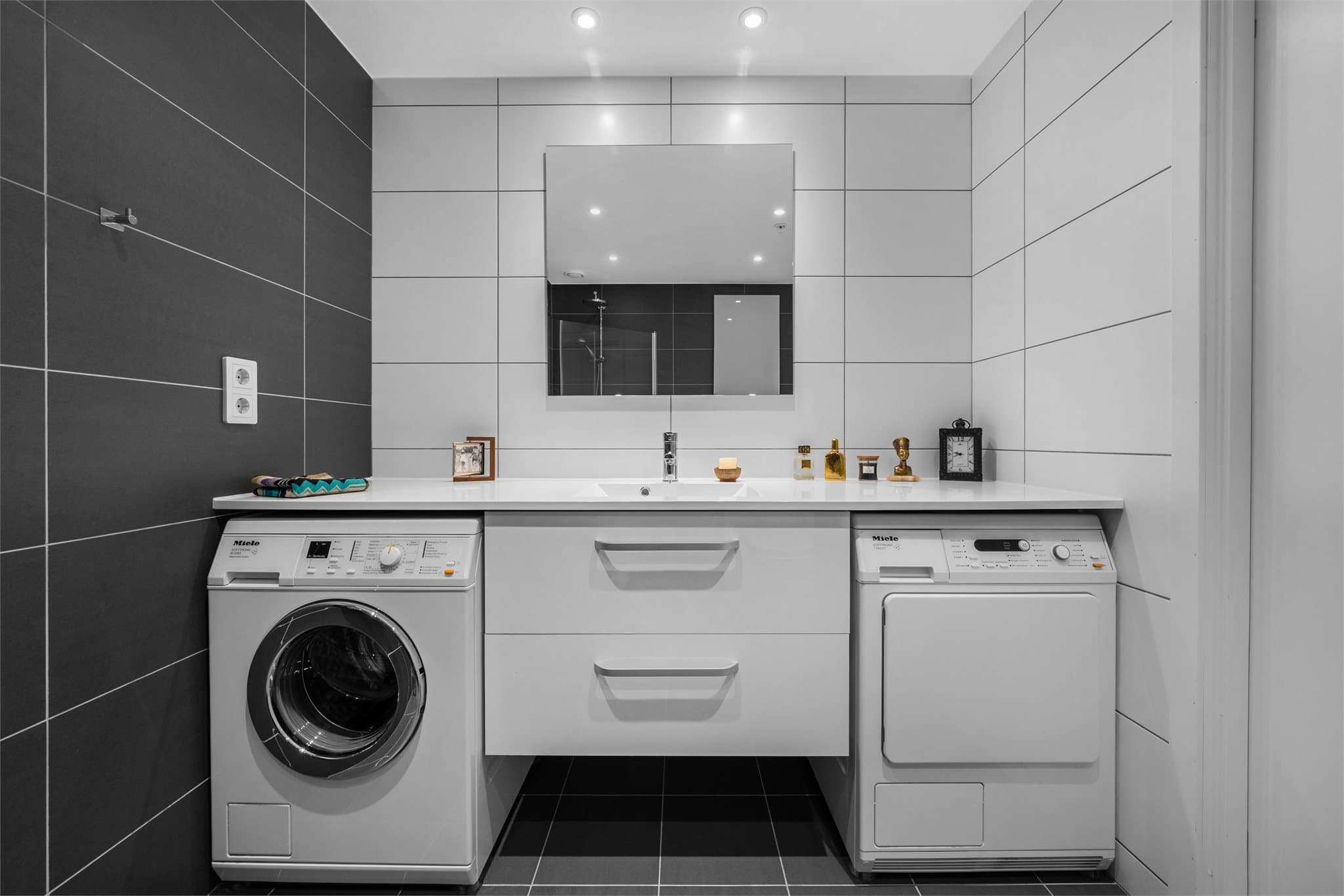 Badet er innredet med helservant på skuffeseksjon, vegghengt toalett og dusjhjørne. Opplegg for vaskemaskin og tørketrommel.