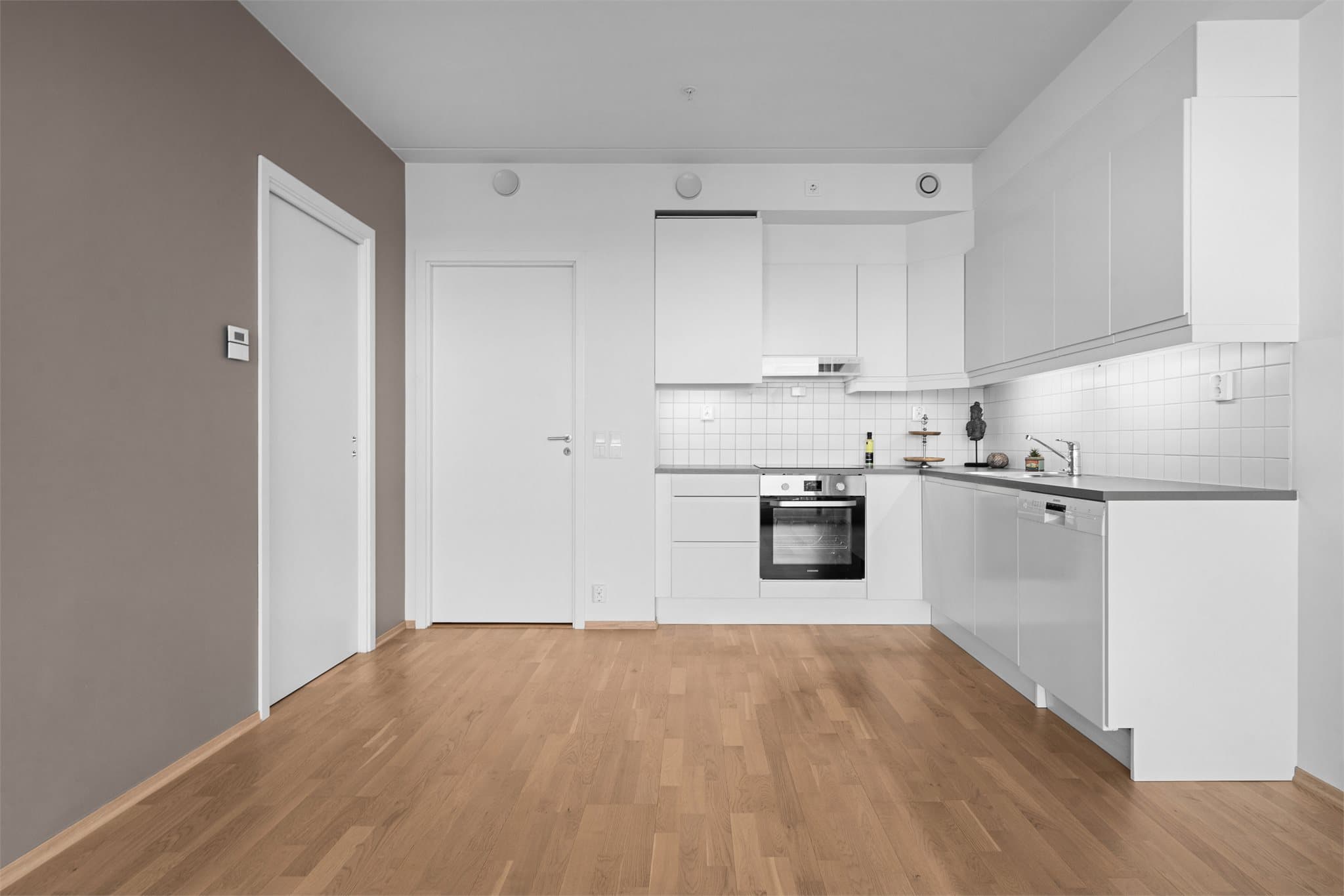 Kjøkkeninnredningen har hvite, slette fronter og laminat benkeplate. Mellom benk og overskap er det fliser.