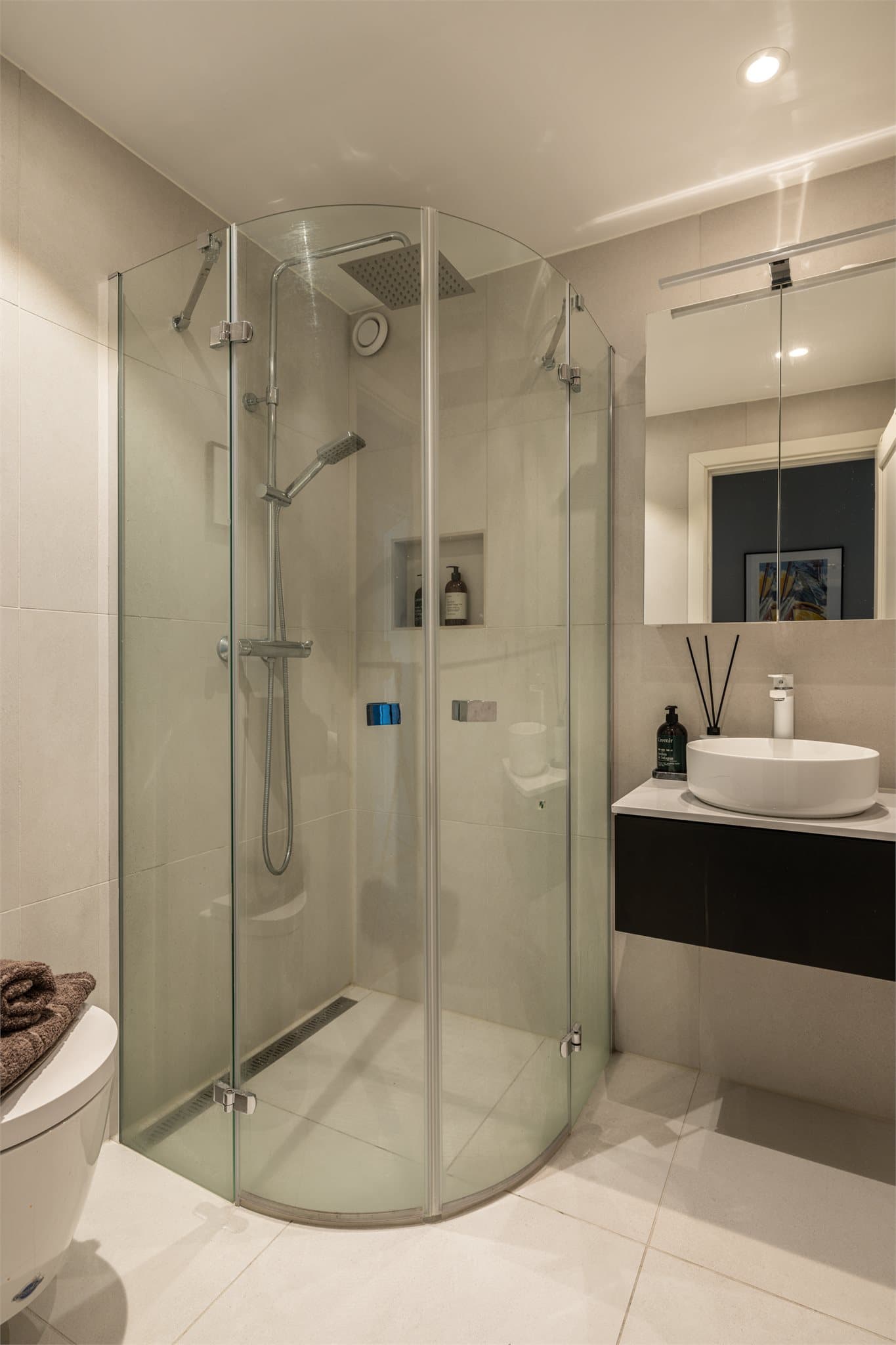 Badet er innredet med dusjhjørne med svingbare glassdører og speilskap med lys.