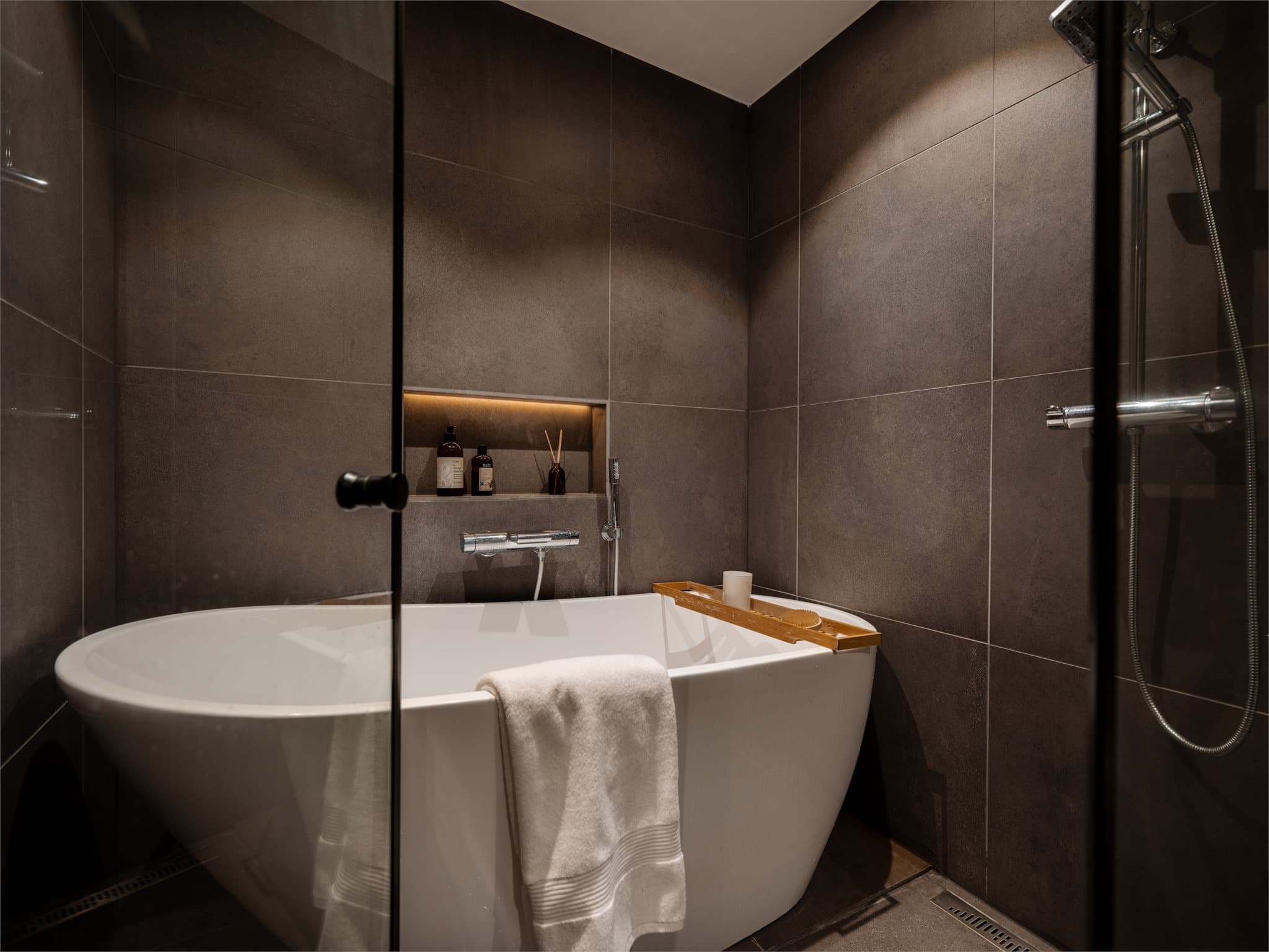 En integrert nisje i flisveggen gir en stilren oppbevaringsløsning ved badekaret.