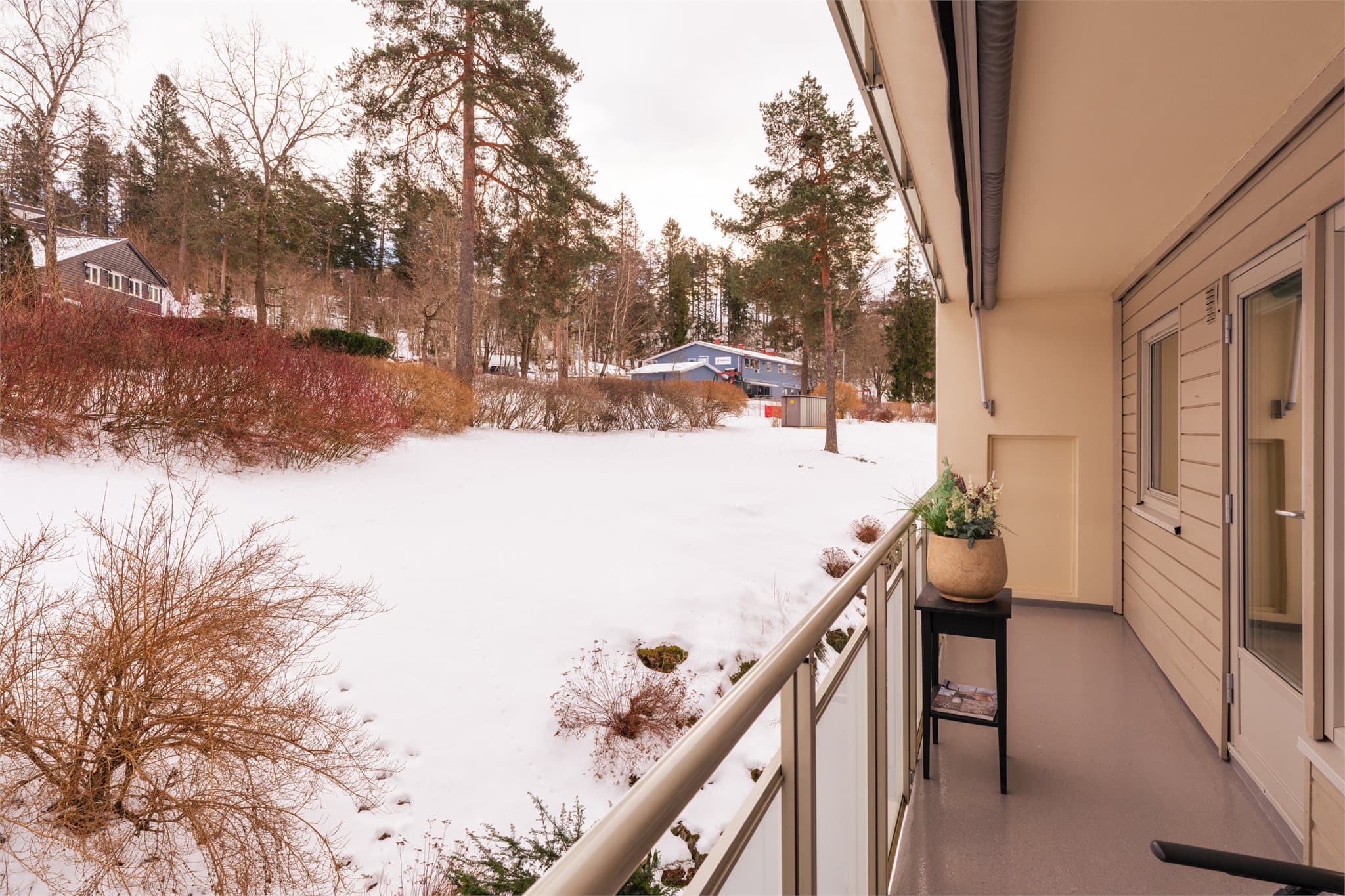 Balkongen har rekkverk med glassfelt og utsikt mot grønne fellesarealer.