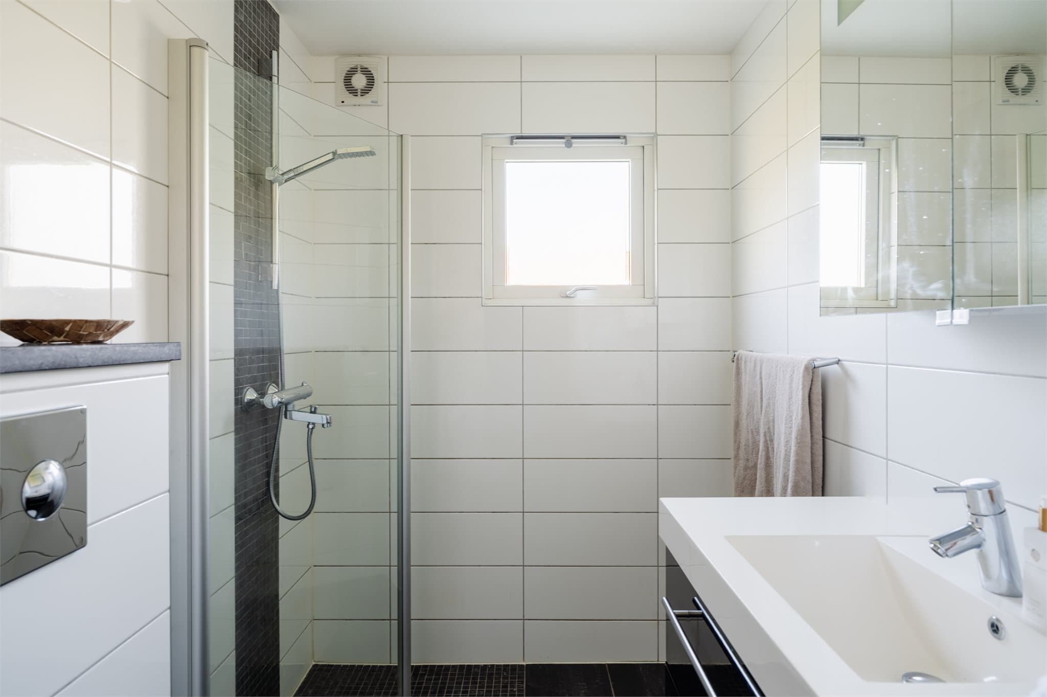 Badet har flislagte overflater, varmekabler i gulv, dusjhjørne, vegghengt toalett og åpningsbart vindu.