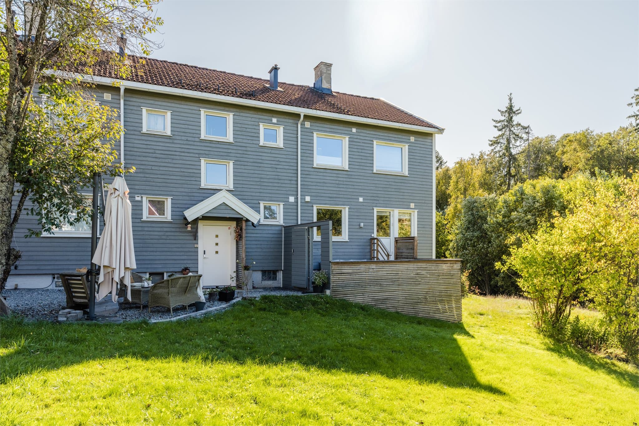 Eiendommen har et overbygget inngangsparti med gruslagt adkomst, felles sitteplass og hyggelige utearealer rundt bygningen.