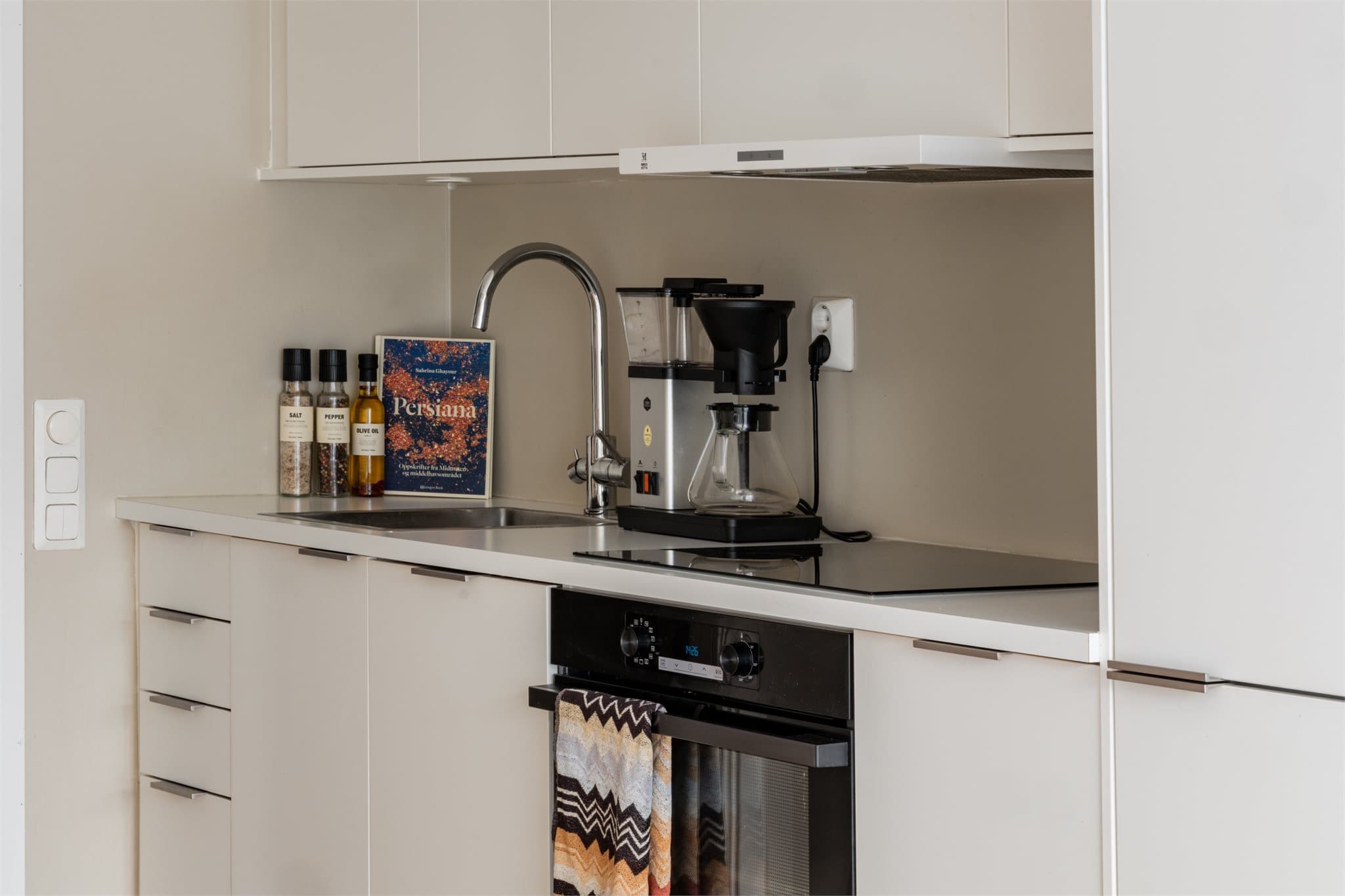 Kjøkkeninnredningen fra Norema har matte hvite fronter og integrerte hvitevarer som medfølger handelen. Downlights i overskap.