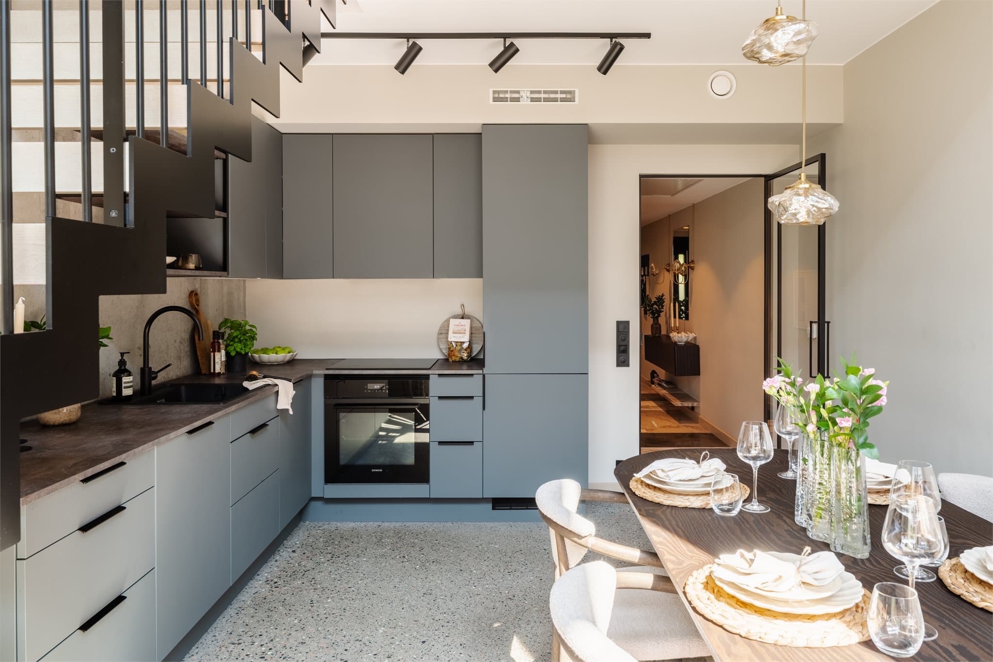 Kjøkkenet ligger i en åpen løsning mot stuen, elegant plassert under trappen til mesaninen. Innredning fra HTH (2024) med glatte fronter og laminat benkeplate.