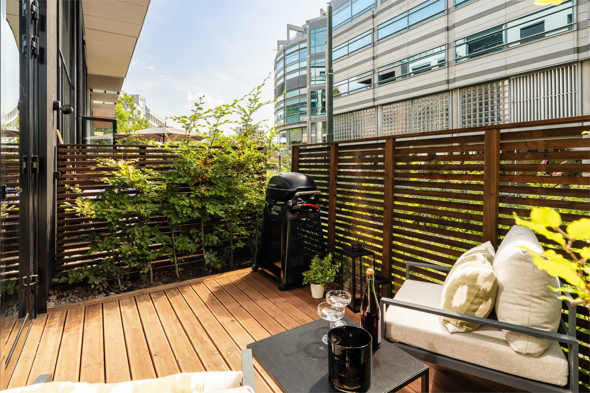 Terrassen har terrassebord på bjelkelag i tre og trespalteskjermer på sidene som gir en lun, hyggelig og skjermet uteplass.