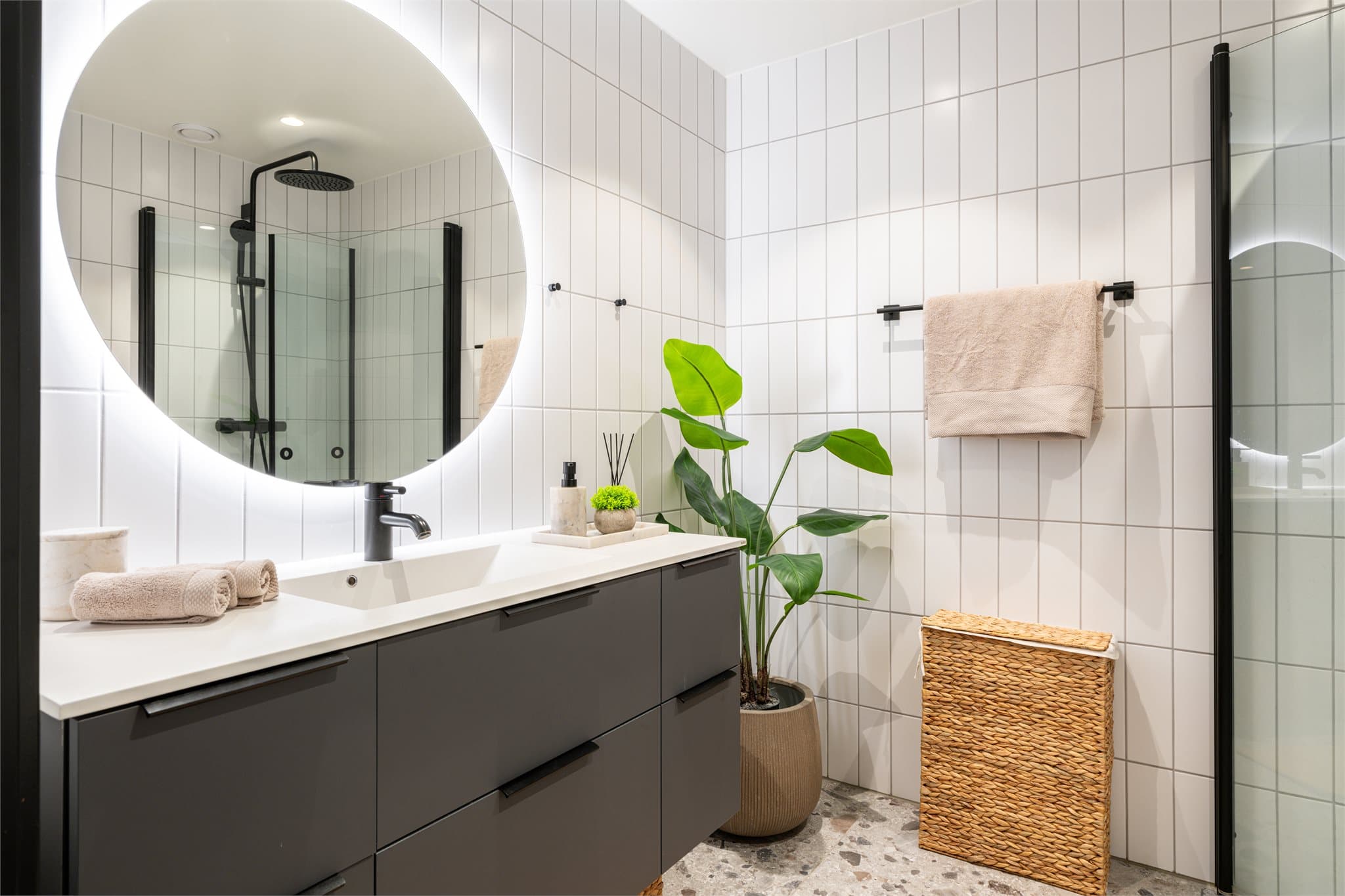Romslig og eksklusivt bad med flislagte vegger og gulv. Gulvet er belagt med store keramiske terrazzo-inspirerte fliser i lyse grå- og beigetoner med natursteinspreg.
