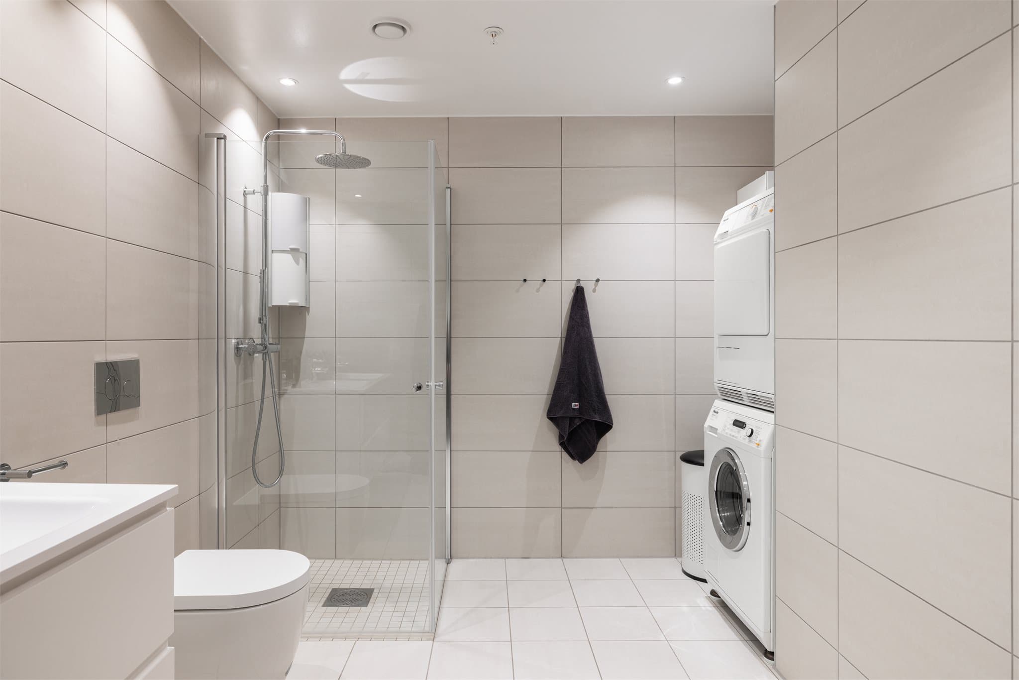 Delikat flislagt bad med elektriske varmekabler og opplegg for vaskemaskin.