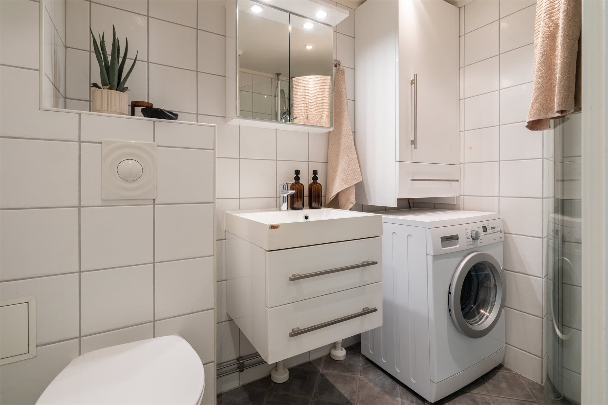 Lyst, flislagt baderom med lun varme i gulvet og opplegg for vaskemaskin.