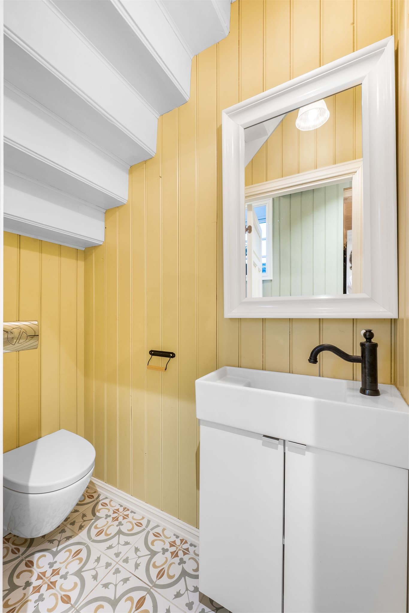 Praktisk toalettrom i 1.etg med flislagt gulv med varmekabler og malt panel i himling og vegger. Rommet er innredet med veggmontert toalett og servant med fabrikklakkerte fronter. Det er speil på vegg over servanten.