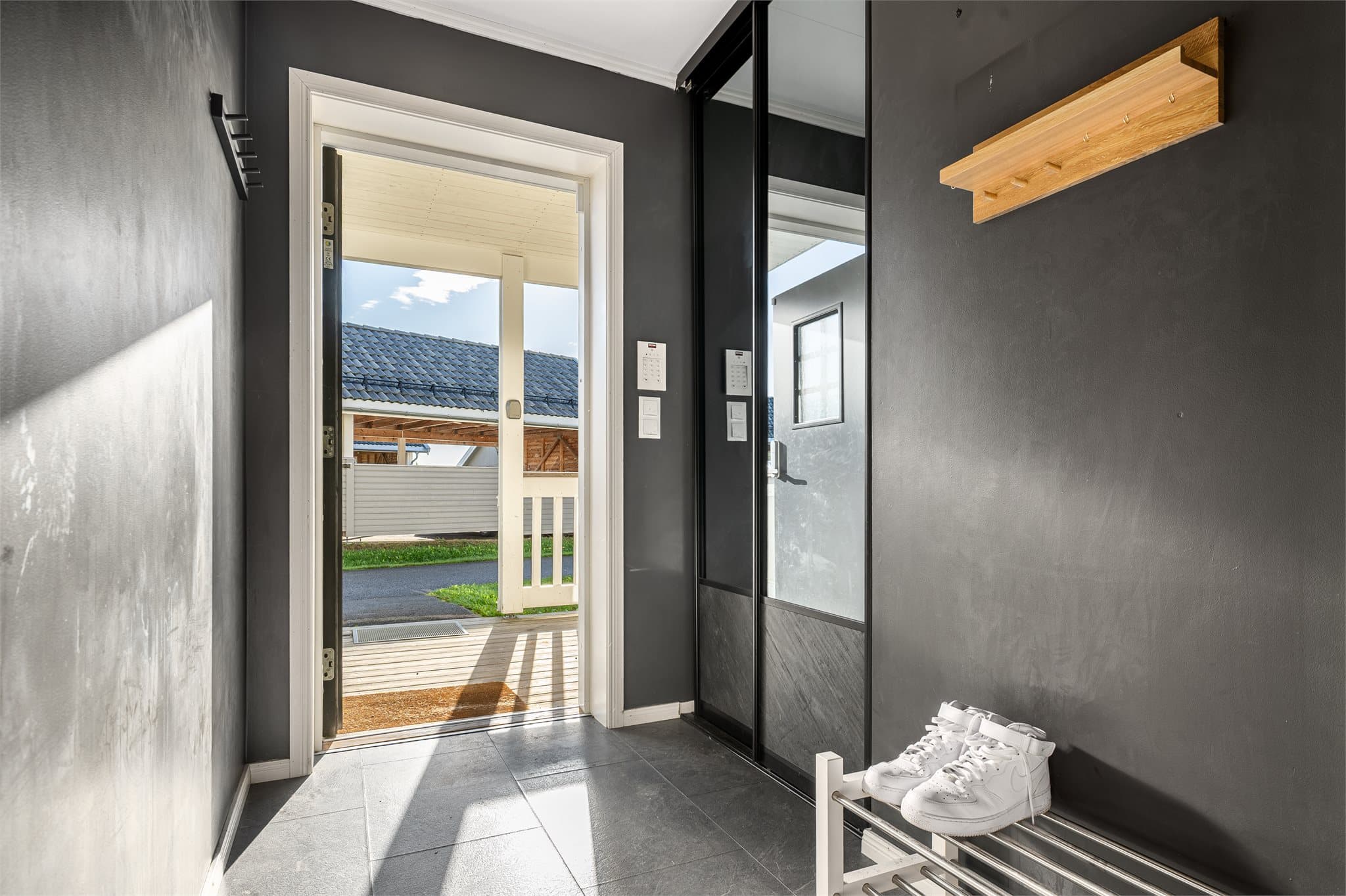 Entréen gir et stilfullt førsteinntrykk med vegger malt i en dempet sort tone som skaper en lun og moderne atmosfære. Her er det god plass til oppbevaring i praktisk skyvedørsgarderobe med speilfronter, som både er funksjonell og romslig.