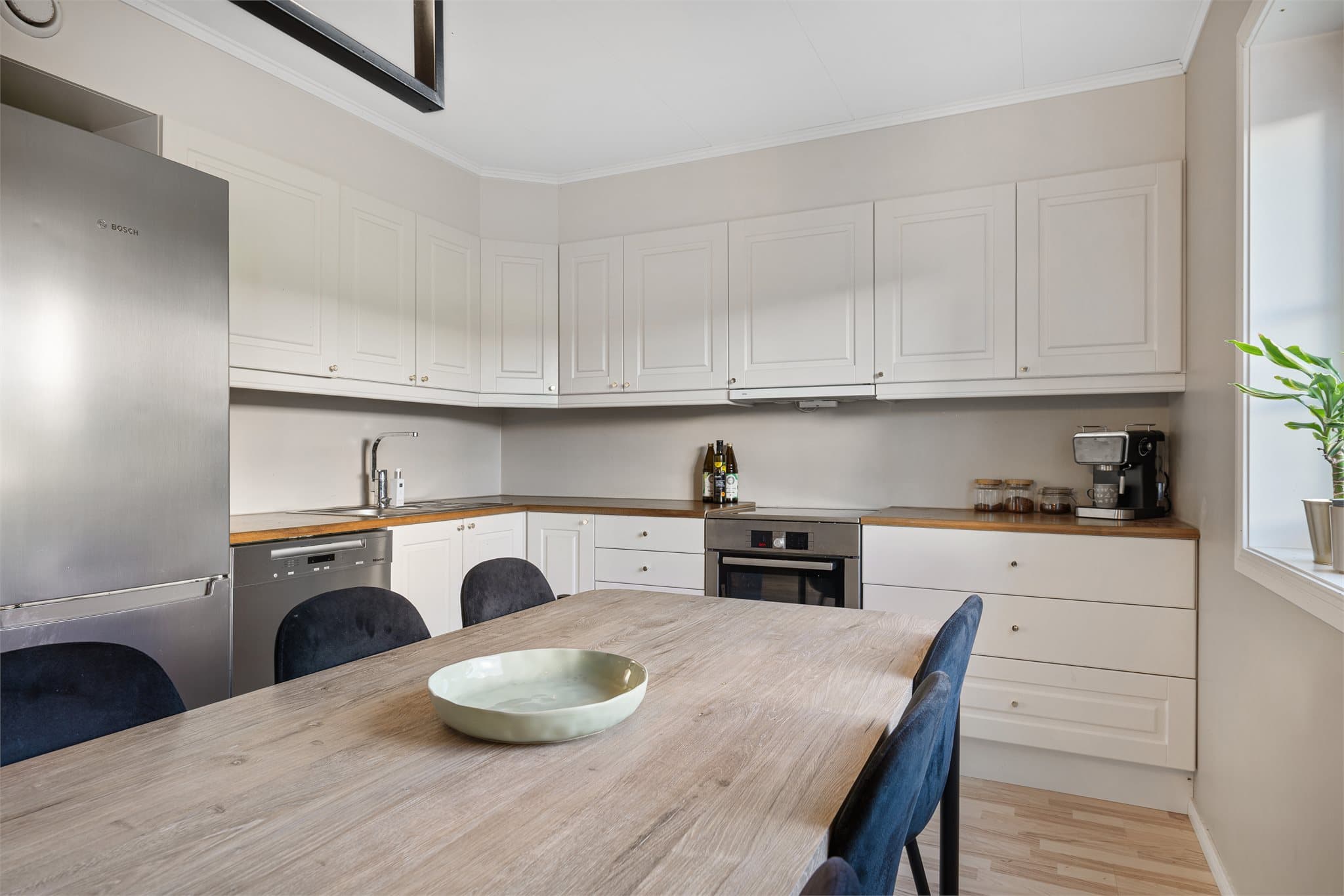 Lyst og klassisk kjøkken med profilerte fronter og god arbeidsplass på laminat benkeplate. Kjøkkenet er praktisk utstyrt med delvis frittstående hvitevarer som komfyr og kombi kjøl/fryseskap.