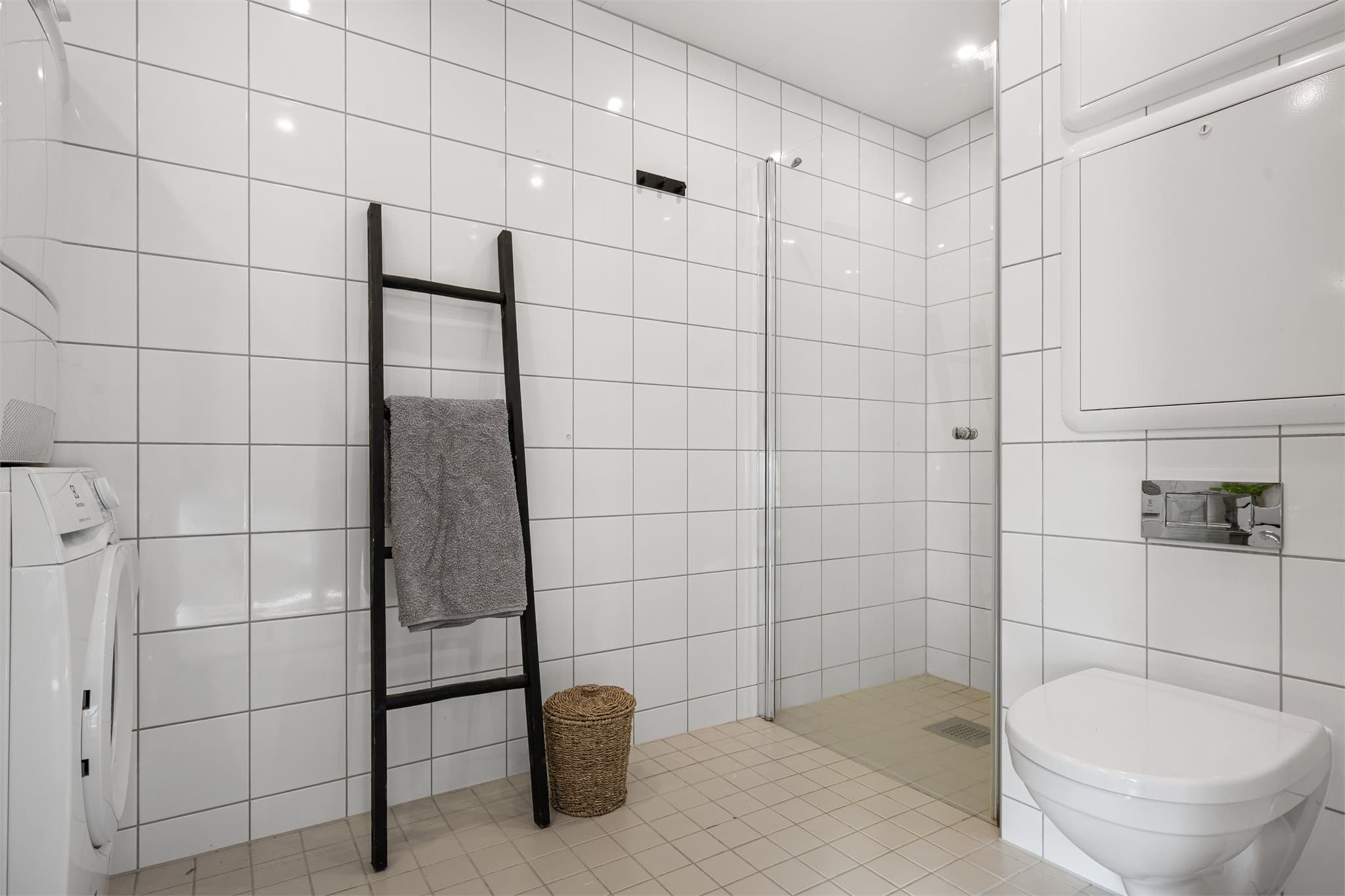 Dusjsonen er etablert i et eget hjørne og avskjermet med dusjdør i herdet glass, noe som gir et ryddig og luftig preg. Utstrakt bruk av downlights i himling.