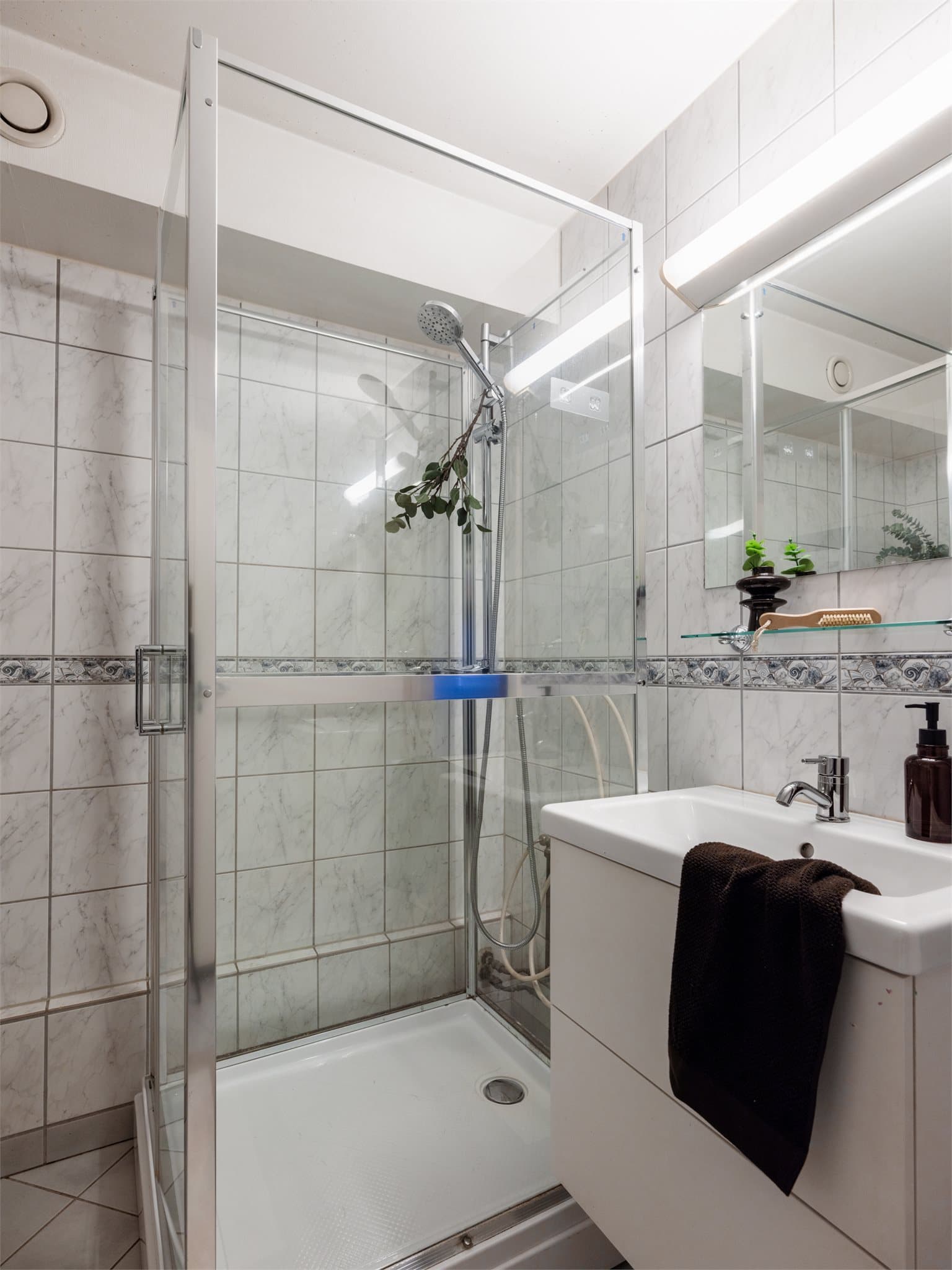 Badet er flislagt og utstyrt med dusjkabinett og servant med underskap.